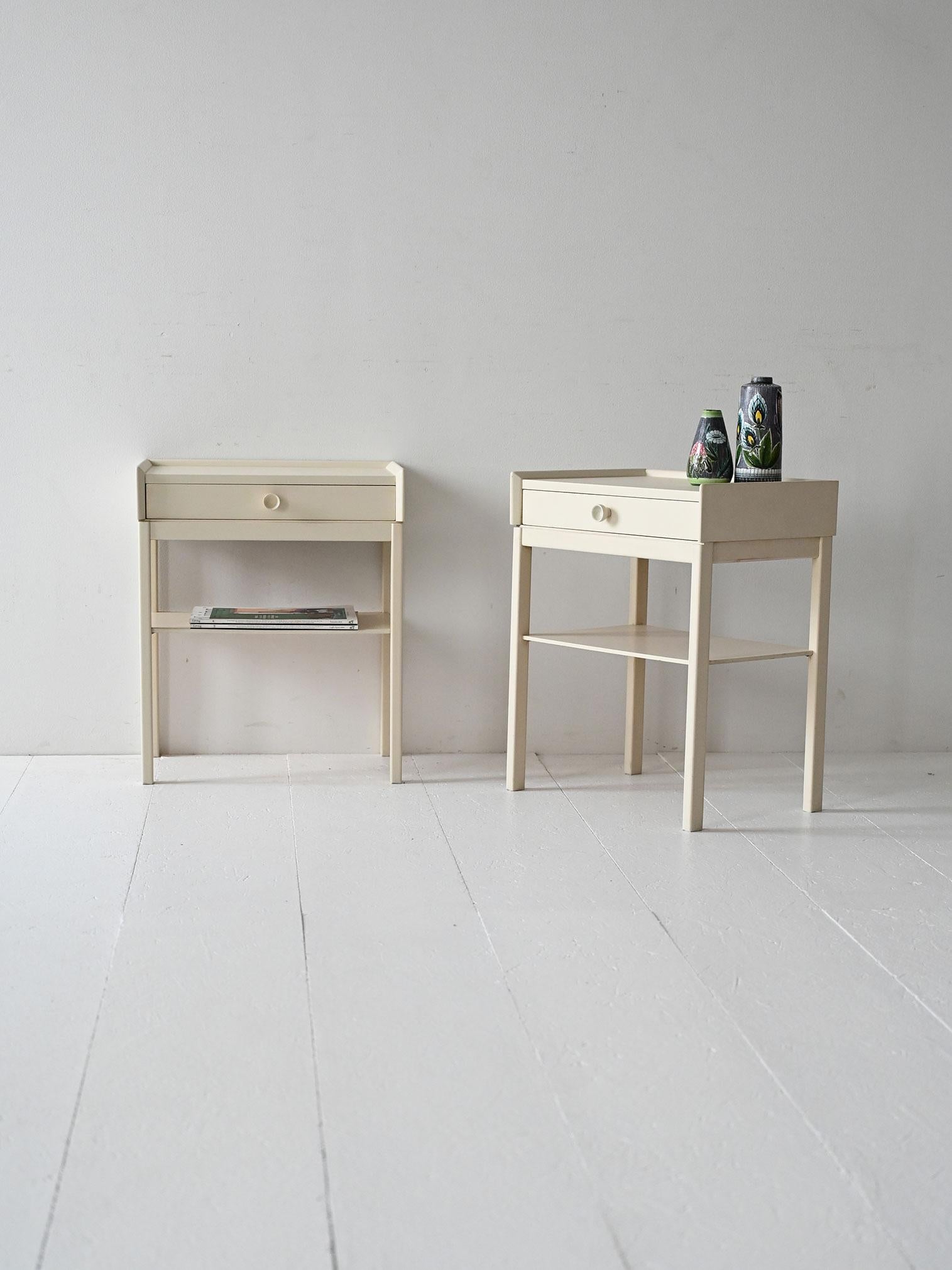Ein Paar weiß lackierte Nachttische im Vintage-Stil mit Schublade, Regal und einfacher Struktur mit klaren, leichten Linien.

Zwei skandinavische Nachttische aus den 1960er Jahren mit weiß lackiertem Holzrahmen. Das minimalistische Design basiert