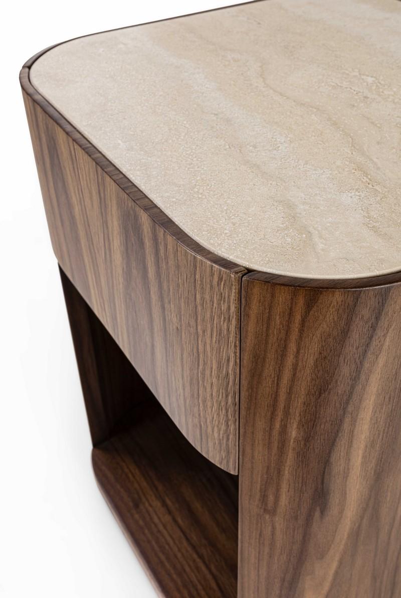Nightstand with simple, rounded lines, presented in Canaletto Walnut and embellished with a matte Travertino marble top. It features a shelf and a drawer with a rallenty system. Also realizable in other wood finishes. Top available in different