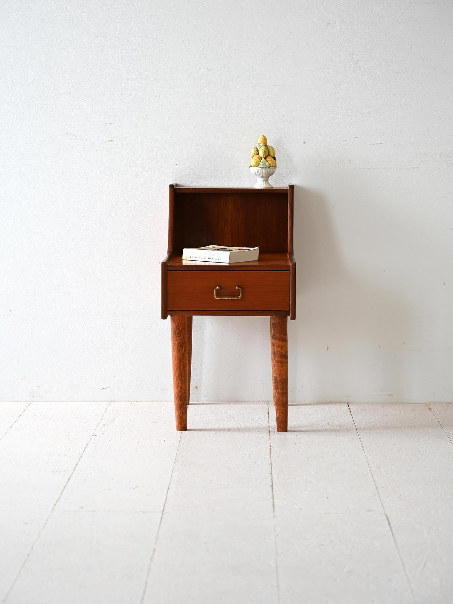 Scandinavian nightstand with drawer and golden metal handle. It features a double tabletop. 

The long tapered legs lend momentum to the structure, while the double shelf provides additional space to display small decorative items or books. 
Good