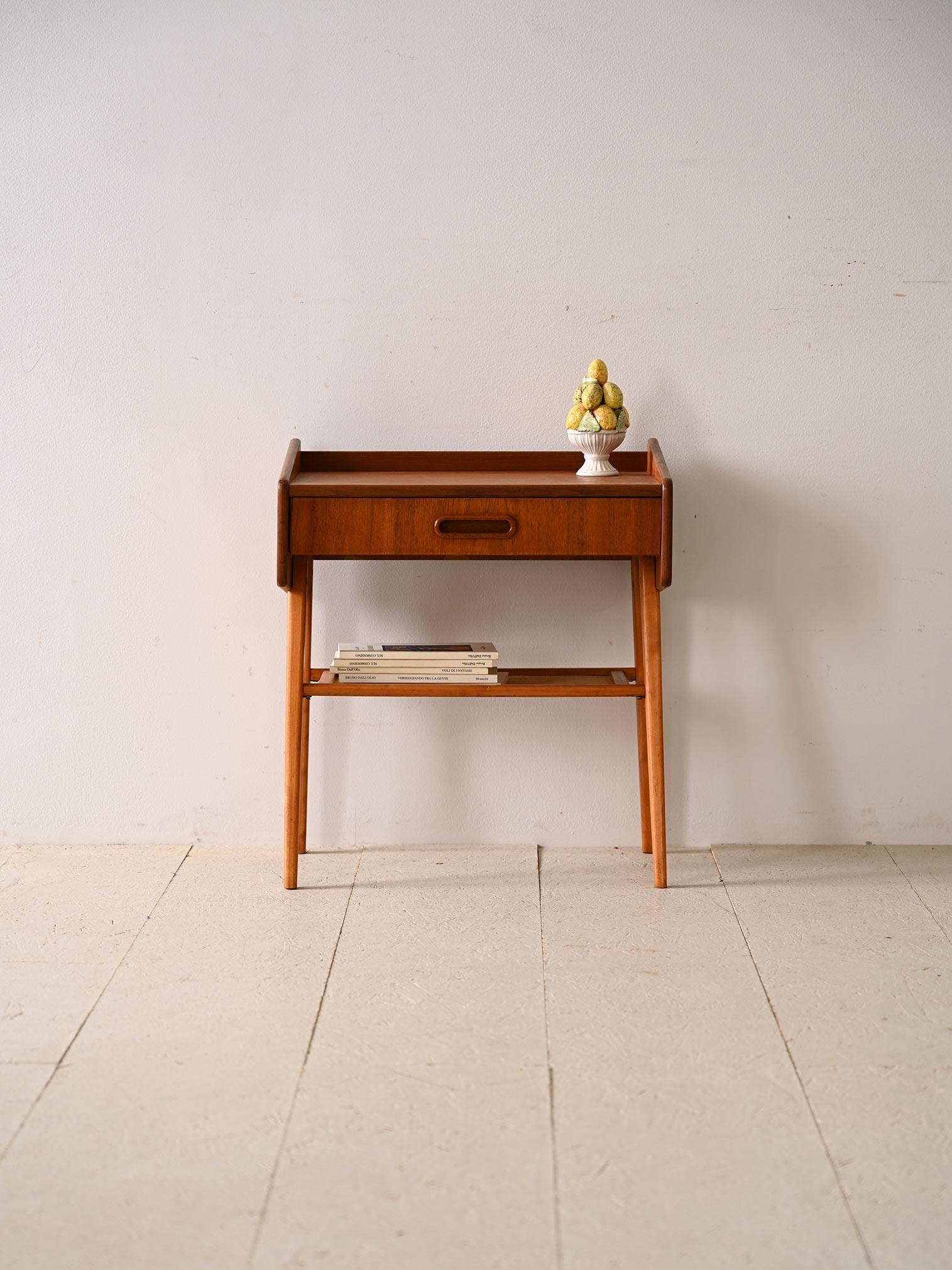 Original vintage nightstand with drawer. Made of fine teak wood, this bedside table embodies the distinctive style of the era with the drawer, equipped with a carved wooden handle, provides space to store small essentials. Slender legs, angled