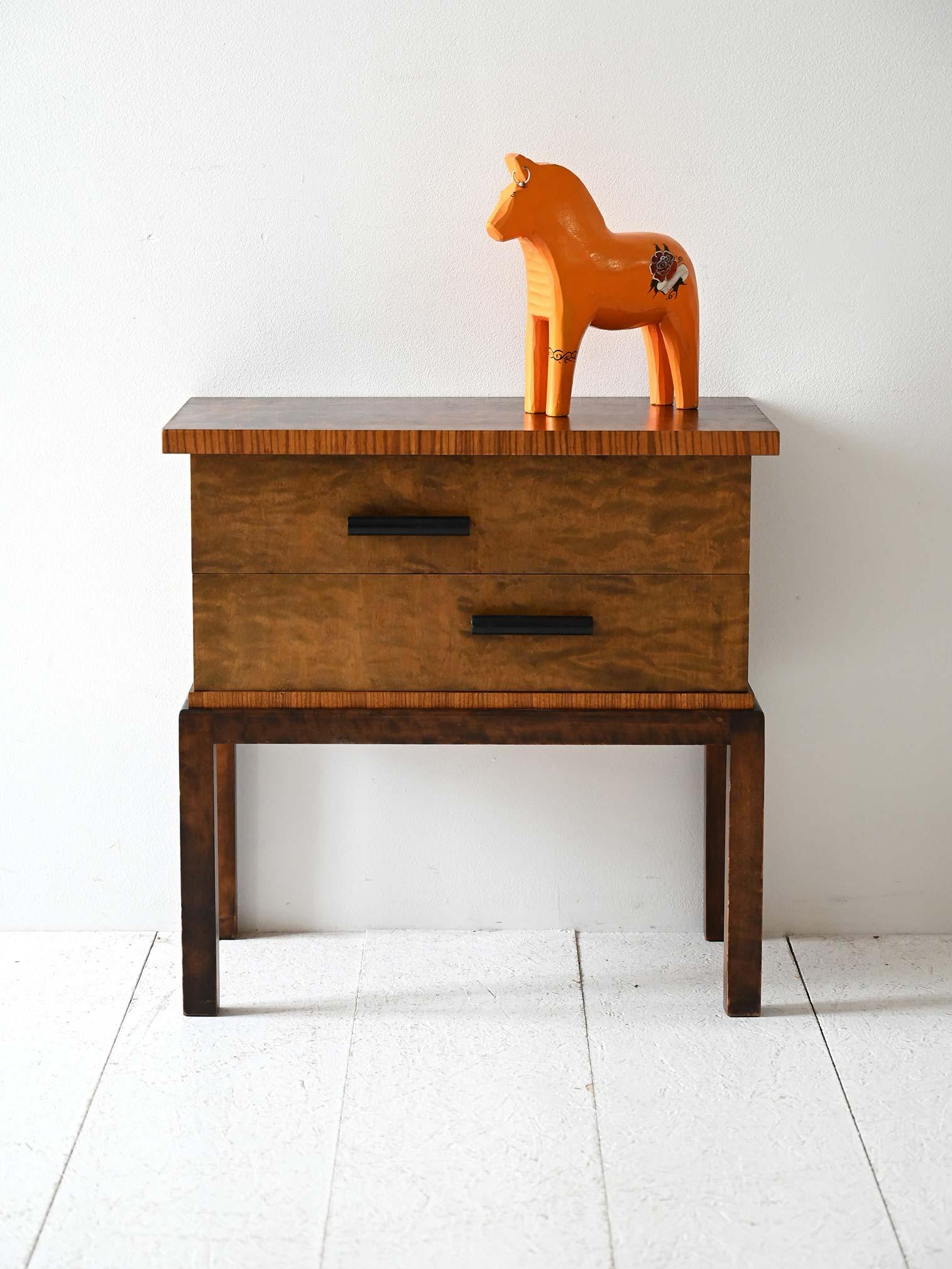 Comodino vintage anni ’30 in radica con inserti a contrasto e due cassetti con maniglie cilindriche nere.

Comodino scandinavo in stile déco risalente agli anni ’30, realizzato in radica fiammata con inserti e bordature a contrasto. La struttura