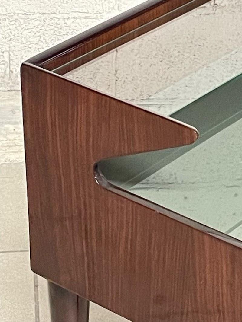 Comodino degli anni '50 in legno di pregio e parti anche in legno tinto.

Top in vetro verde con mensolina in vetro trasparente oltre a particolari in ottone.

Il comodino non è restaurato ma si presenta in buone condizioni.    