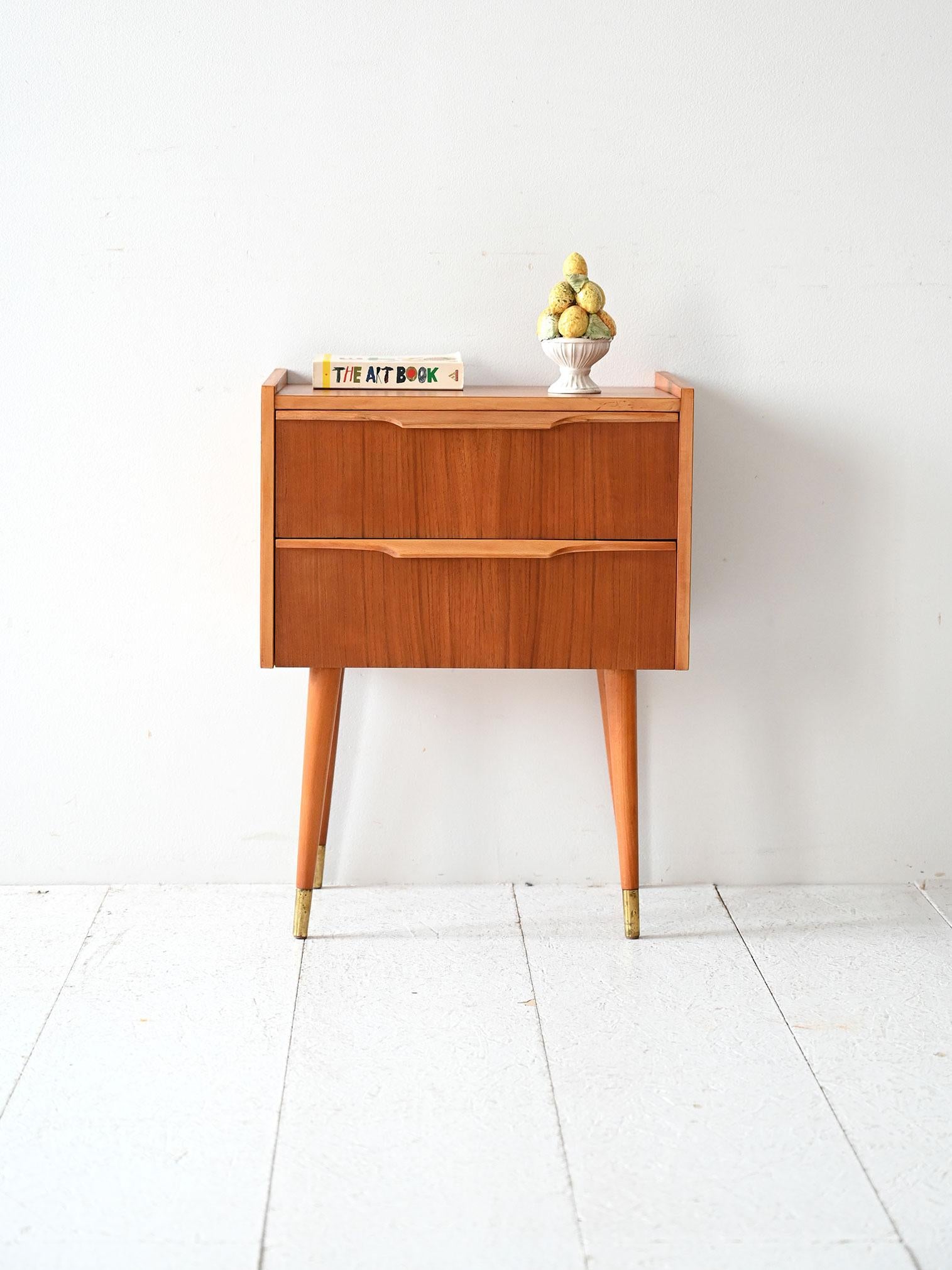 Comodino vintage con due cassetti, maniglie scolpite, gambe affusolate e inserti in ottone. Teak con essenze a contrasto.

Comodino scandinavo degli anni ’50 realizzato in teak con eleganti essenze a contrasto. Dotato di due cassetti capienti e