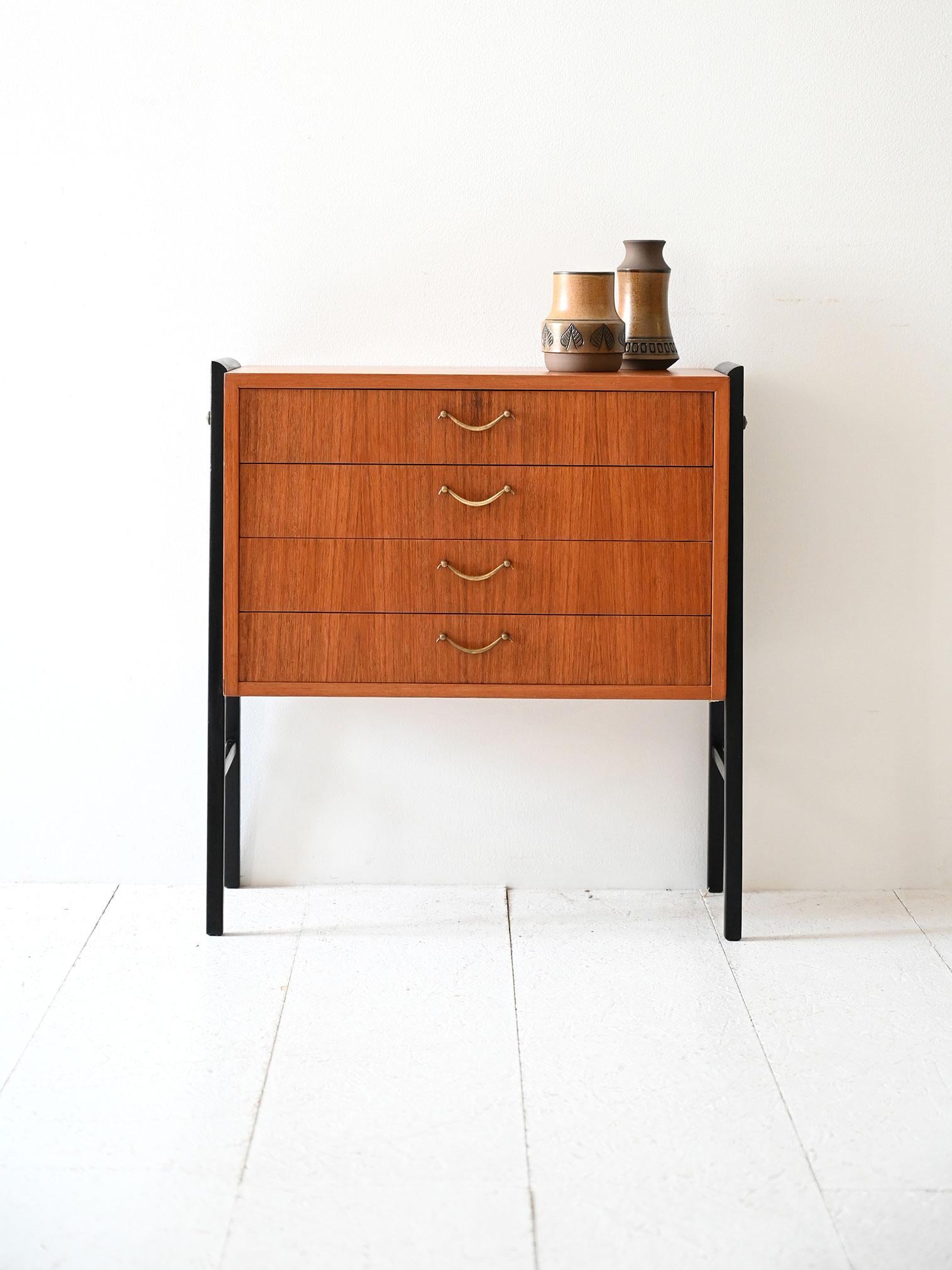 Comodino vintage in teak con quattro cassetti, maniglie in ottone e gambe nere inclinate a cavalletto.

Comodino scandinavo degli anni ’50, realizzato in teak con quattro cassetti dotati di maniglie sagomate in ottone. La struttura è sorretta da
