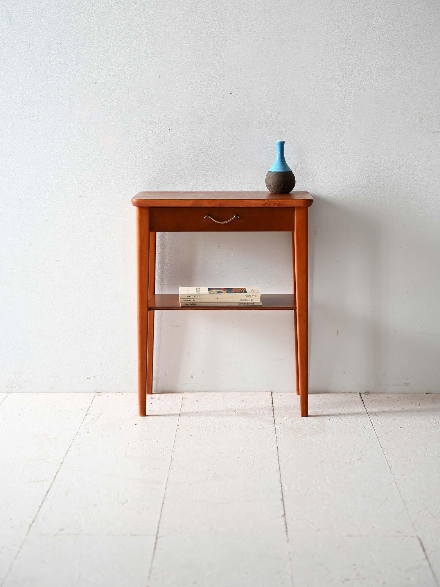 Vintage 1950s teak bedside table with mahogany shelf, tapered legs, drawer with brass handle, and magazine shelf.

Scandinavian 1950s teak bedside table with elegant mahogany lower shelf and slender frame on tapered legs. A front drawer with a brass