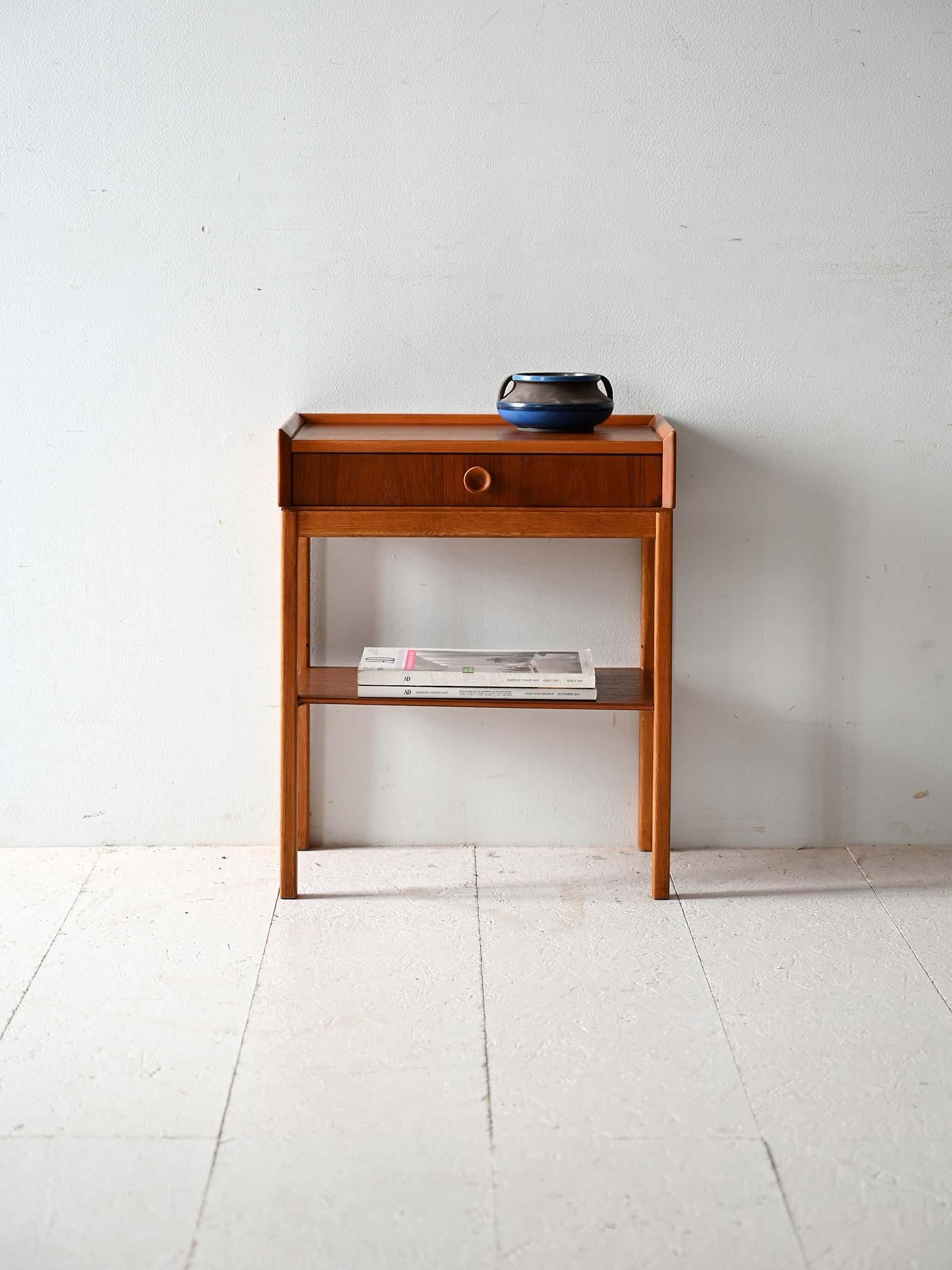 Scandinavian vintage 1960s teak and oak nightstand, drawer with two-tone cylindrical handle and shelf, raised top edge.

Scandinavian 1960s teak and oak bedside table with a drawer fitted with a two-tone cylindrical handle and lower shelf. The edge