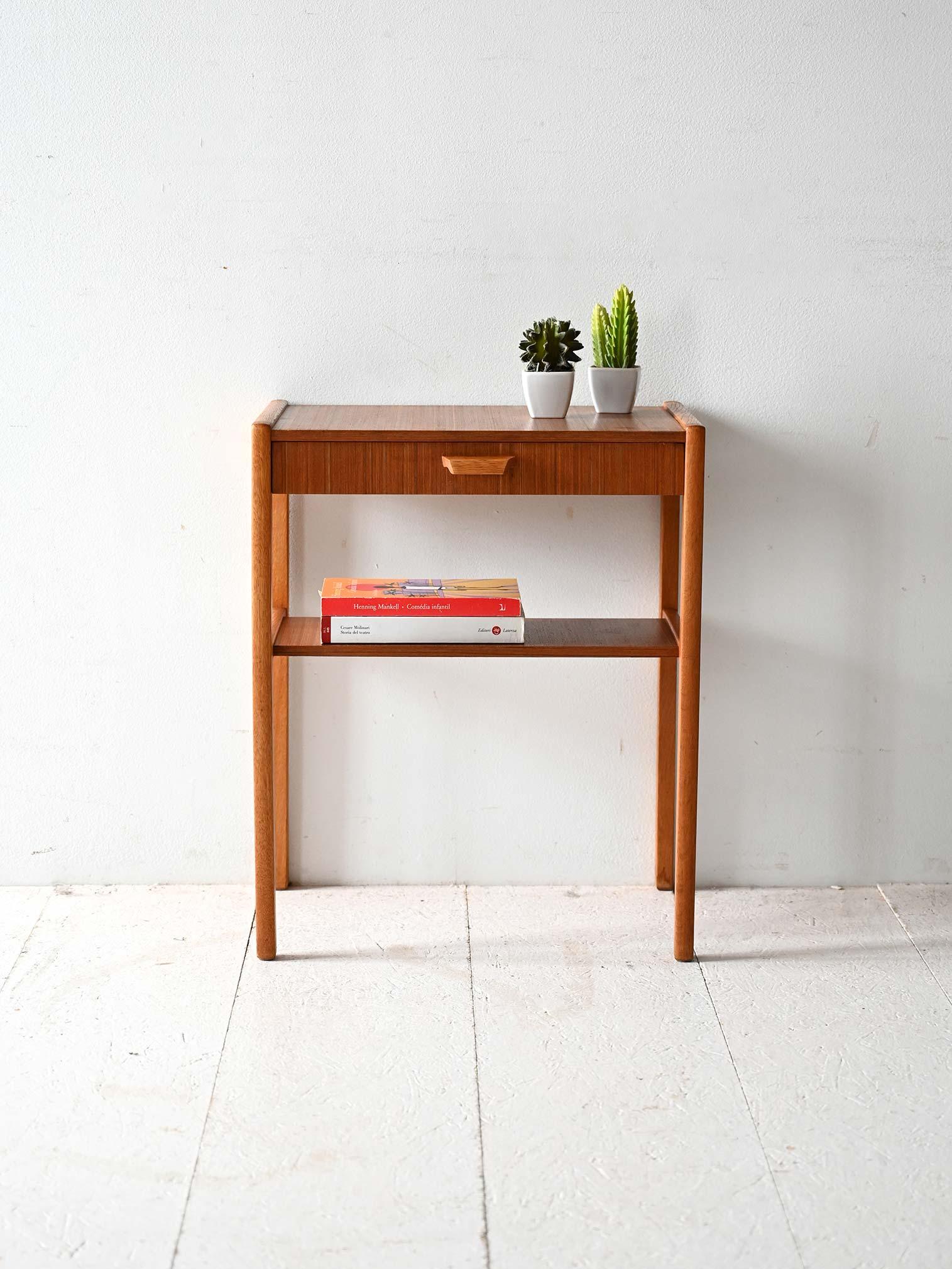Vintage teak bedside table with carved handle, built-in drawer and lower shelf. Linear design and light proportions.

Original Scandinavian nightstand from the 1960s made of teak with a lightweight frame and essential profile. The front drawer