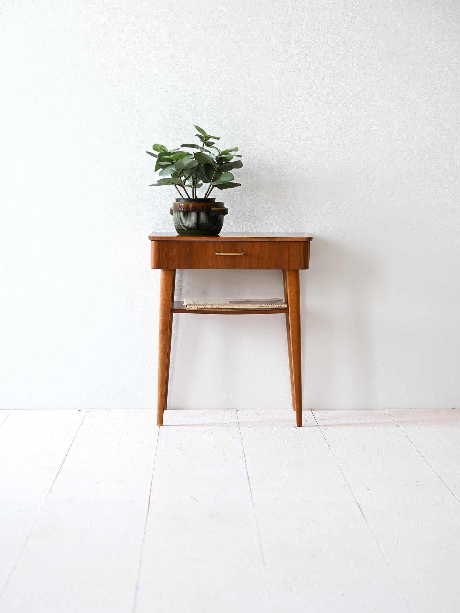 1960s nightstand  features a table top with rounded corners.  Under the top is a drawer with a square metal handle. Below the drawer, there is a magazine shelf, perfect for storing books or newspapers, 

Tapered, tapered and slightly sloping legs