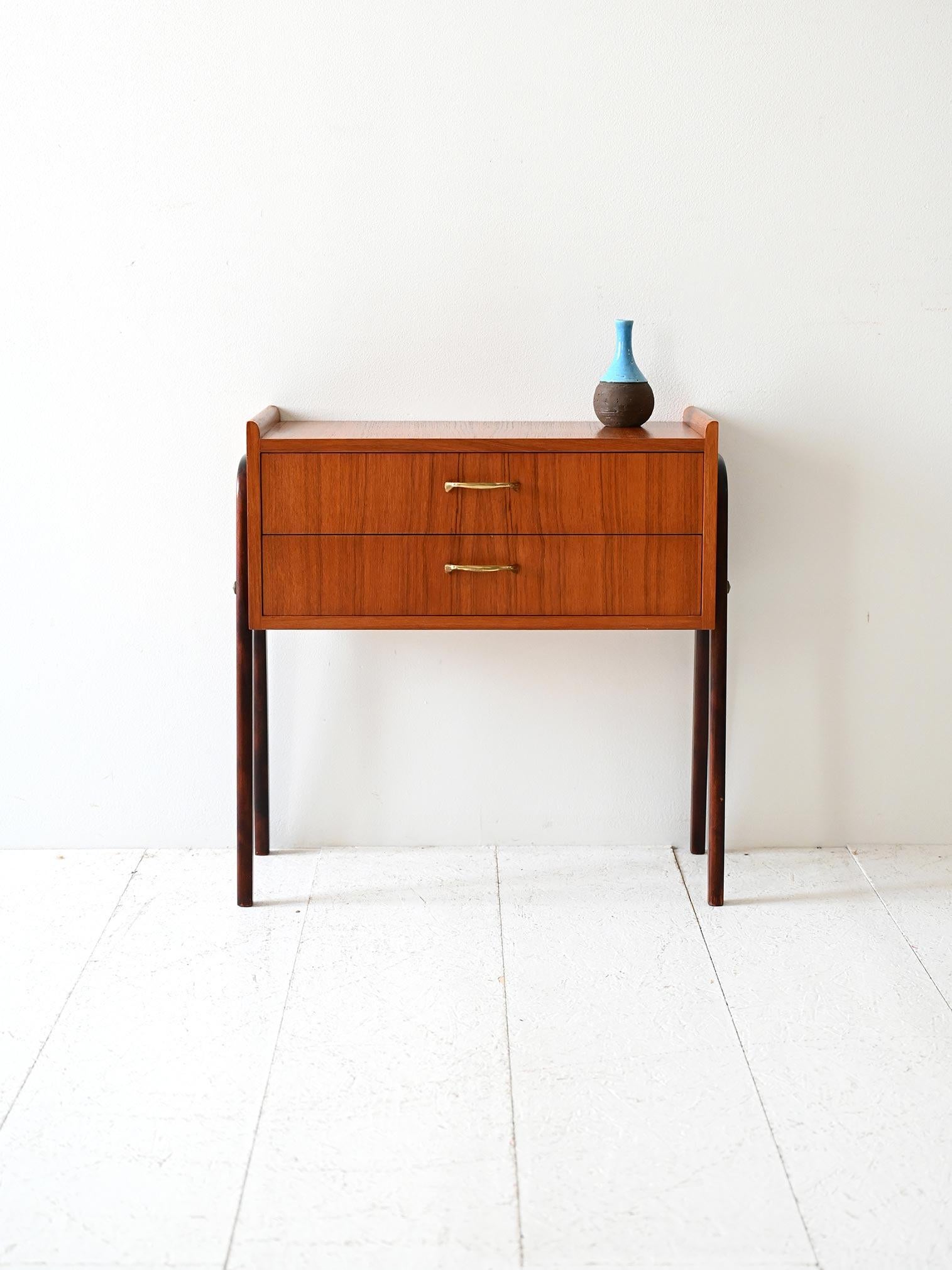 Comodino anni ’50 in teak con due cassetti, maniglie in ottone e gambe in legno scuro lucido a contrasto.

Comodino scandinavo vintage risalente agli anni ’50, realizzato in teak con finitura calda e venatura regolare. Il mobile è dotato di due