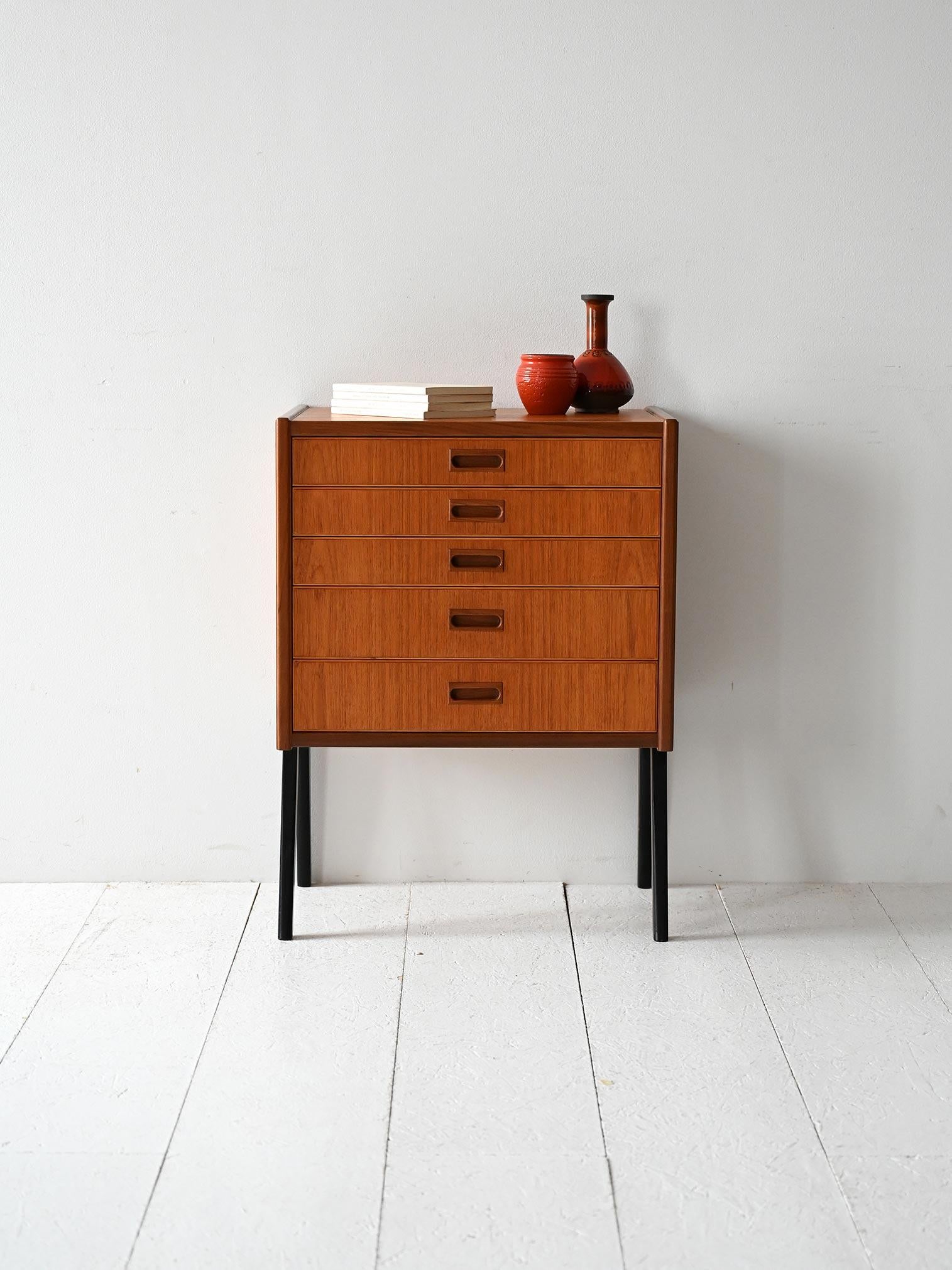 Comodino in legno chiaro e scuro, cinque cassetti con maniglie squadrate e gambe laccate nere.

Comodino scandinavo vintage con cinque cassetti e struttura in legno con venature a contrasto. Le maniglie hanno un profilo squadrato intagliato nel