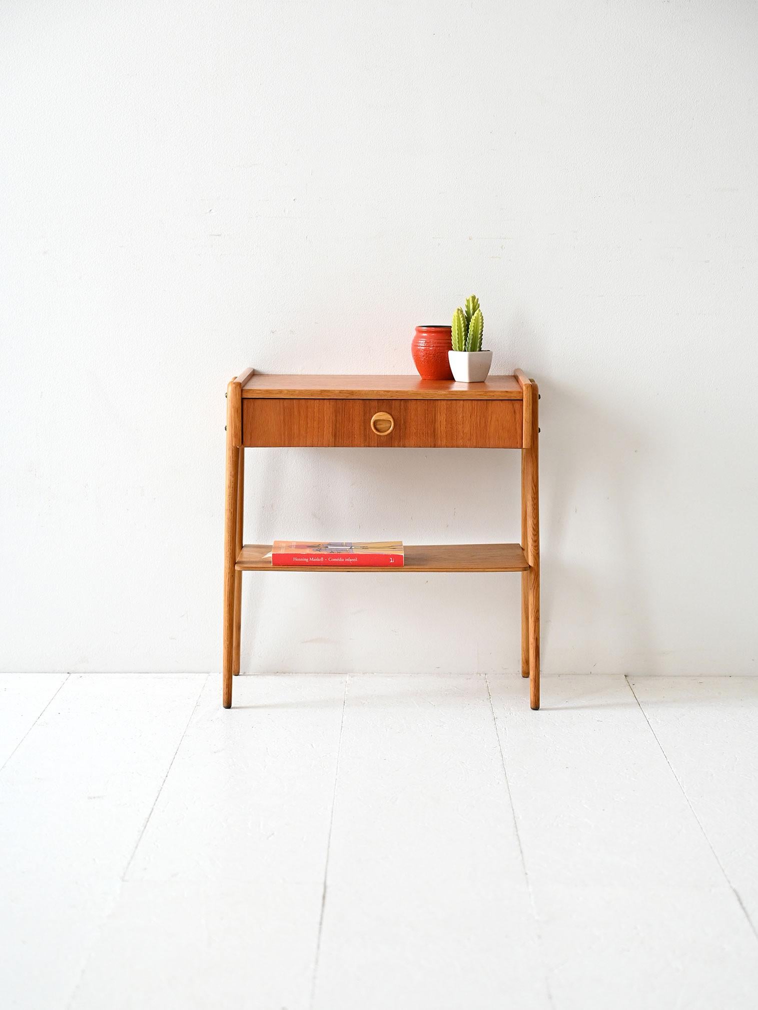 Comodino in teak con gambe inclinate a V, cassetto con maniglia intagliata e ripiano inferiore. Design essenziale nordico.

Comodino scandinavo in teak degli anni ’50/’60 con gambe sottili inclinate a V verso il basso. La struttura compatta è