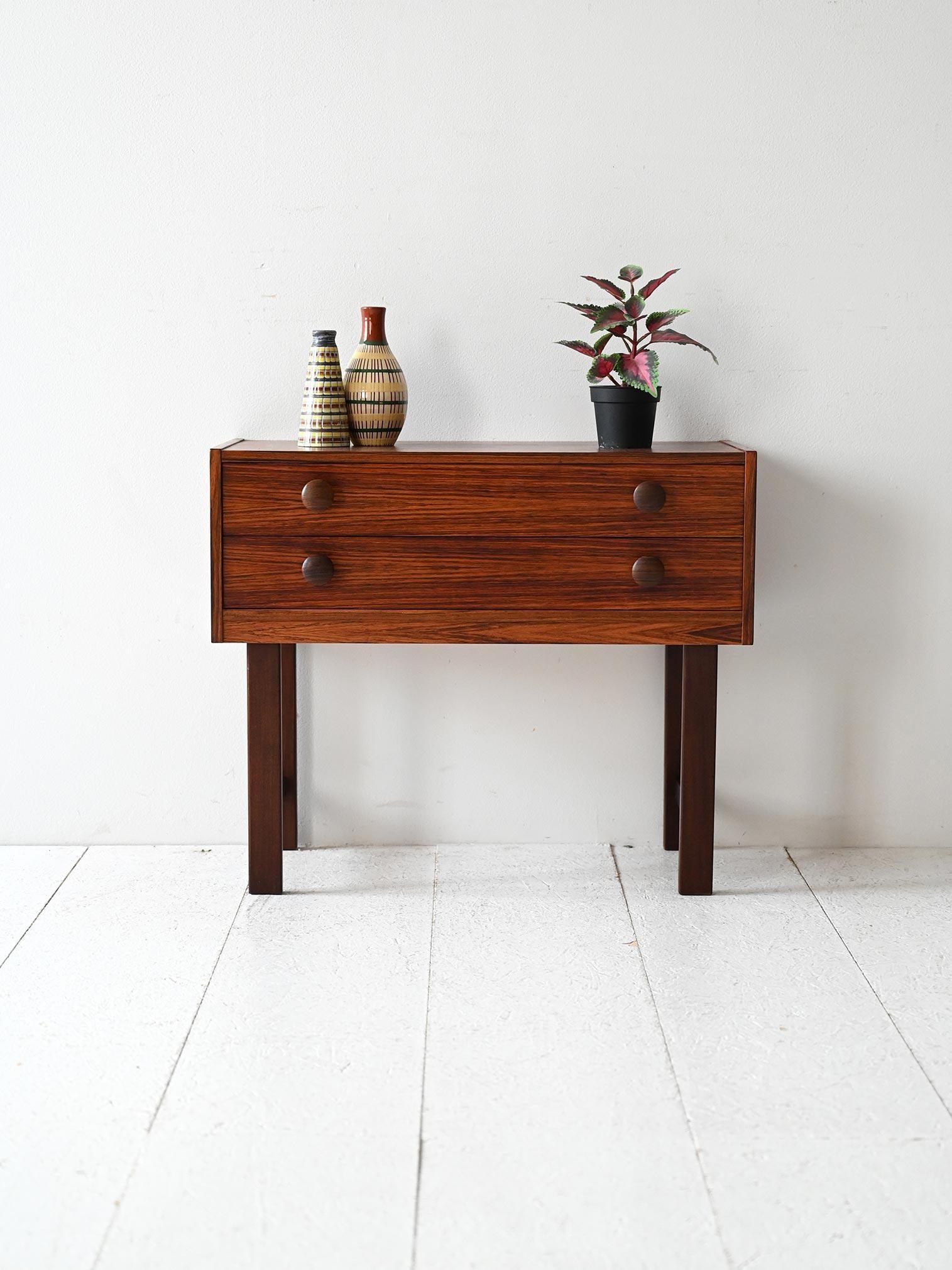 Elegant 1960s rosewood bedside table with two drawers, round handles, and tall, light frame.

Scandinavian 1960s nightstand with two drawers, made of fine rosewood, a rare wood prized for its deep grain and warm tone. The round handles echo the same