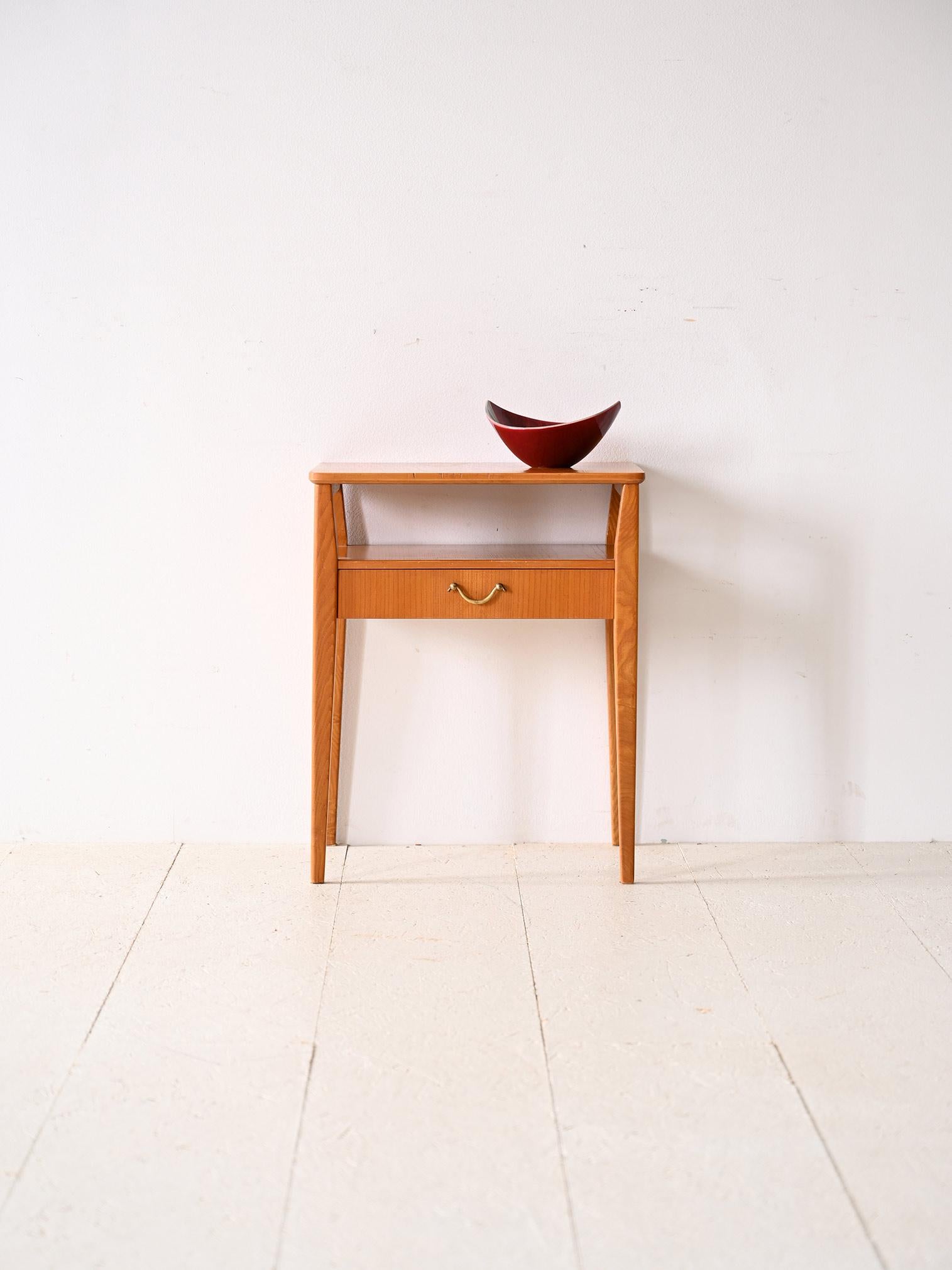 Scandinavian teak and birch bedside table.

This 1960s coffee table recalculates the style and taste of mid-century Nordic design. Consisting of a double shelf and equipped with a drawer with a gold metal handle, it is ideal as a bedside table as
