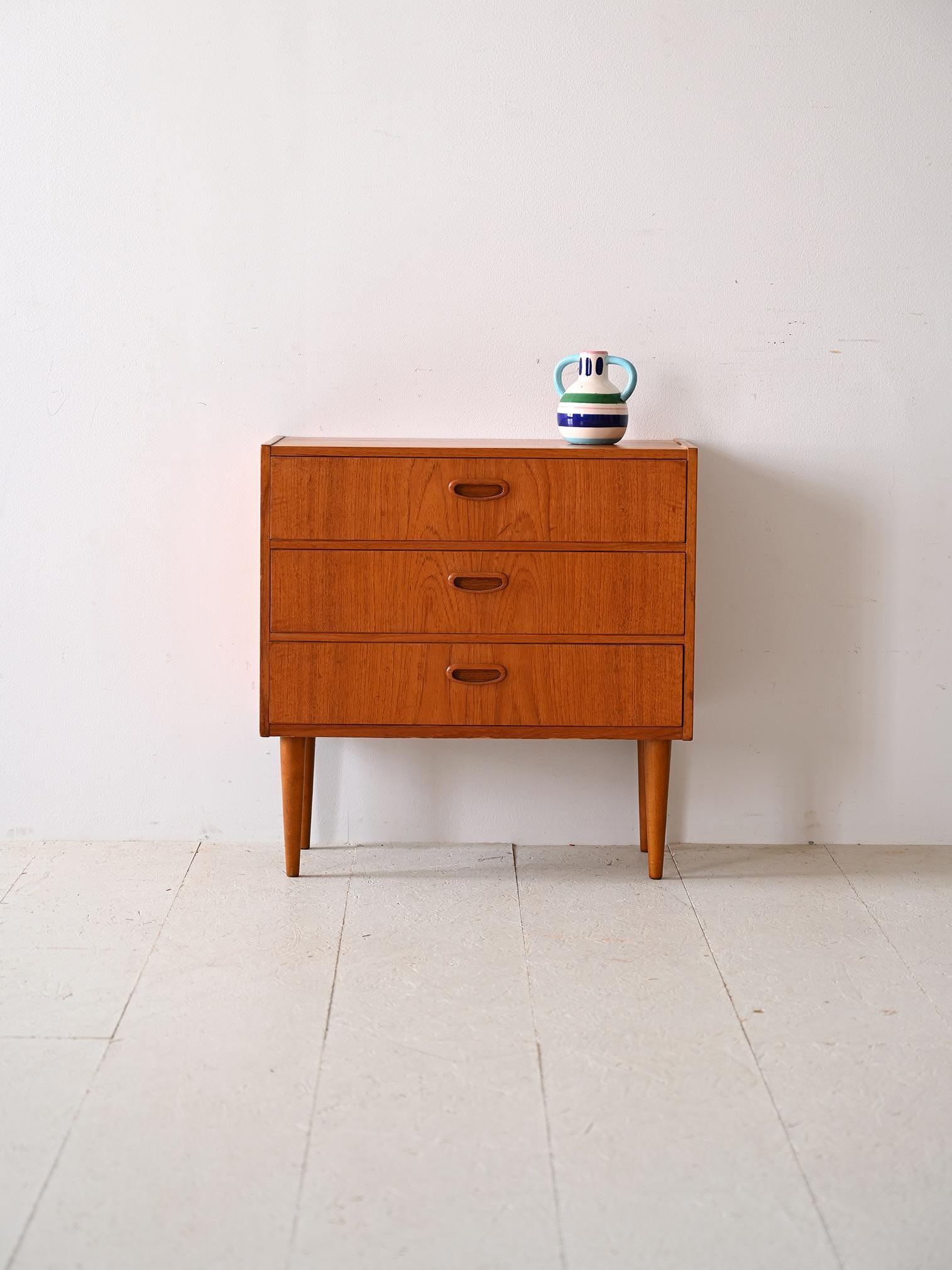 Small original 1960s Danish style chest of drawers.

The linear frame features three drawers with wood-carved handles and is supported by tapered legs that emphasize its lightness.
Despite its small size, it is designed to maximize storage space