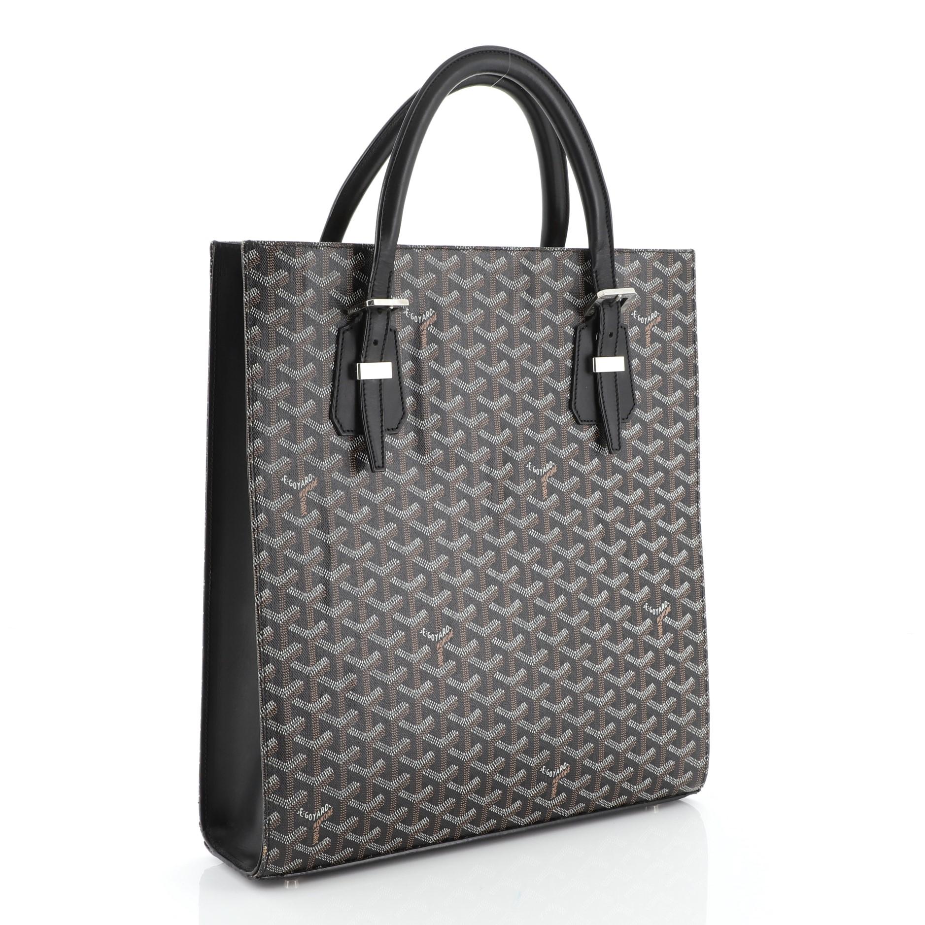 This Goyard Comores Tote Coated Canvas GM, crafted from brown coated canvas, features dual leather handles with buckle detailing, leather trim, protective base studs and silver-tone hardware. It opens to a yellow fabric interior with side zip