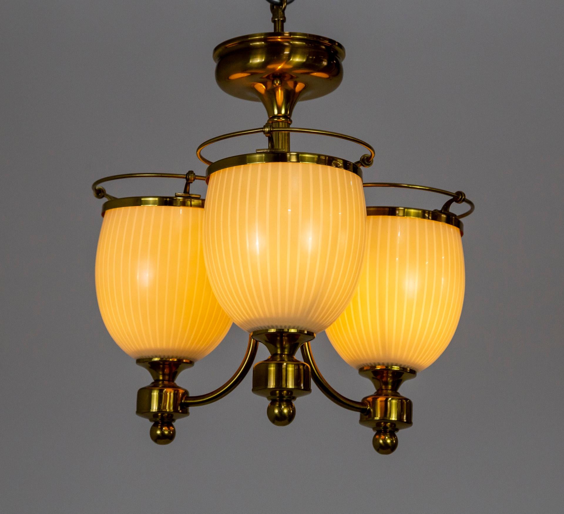 A brass chandelier in a compact design with three up-lights.  The cream glass shades have subtle stripes and are rimmed with open brass wire caps. A versatile design to fit multiple decors. Contemporary.  Newly made with new and vintage parts. 14.5