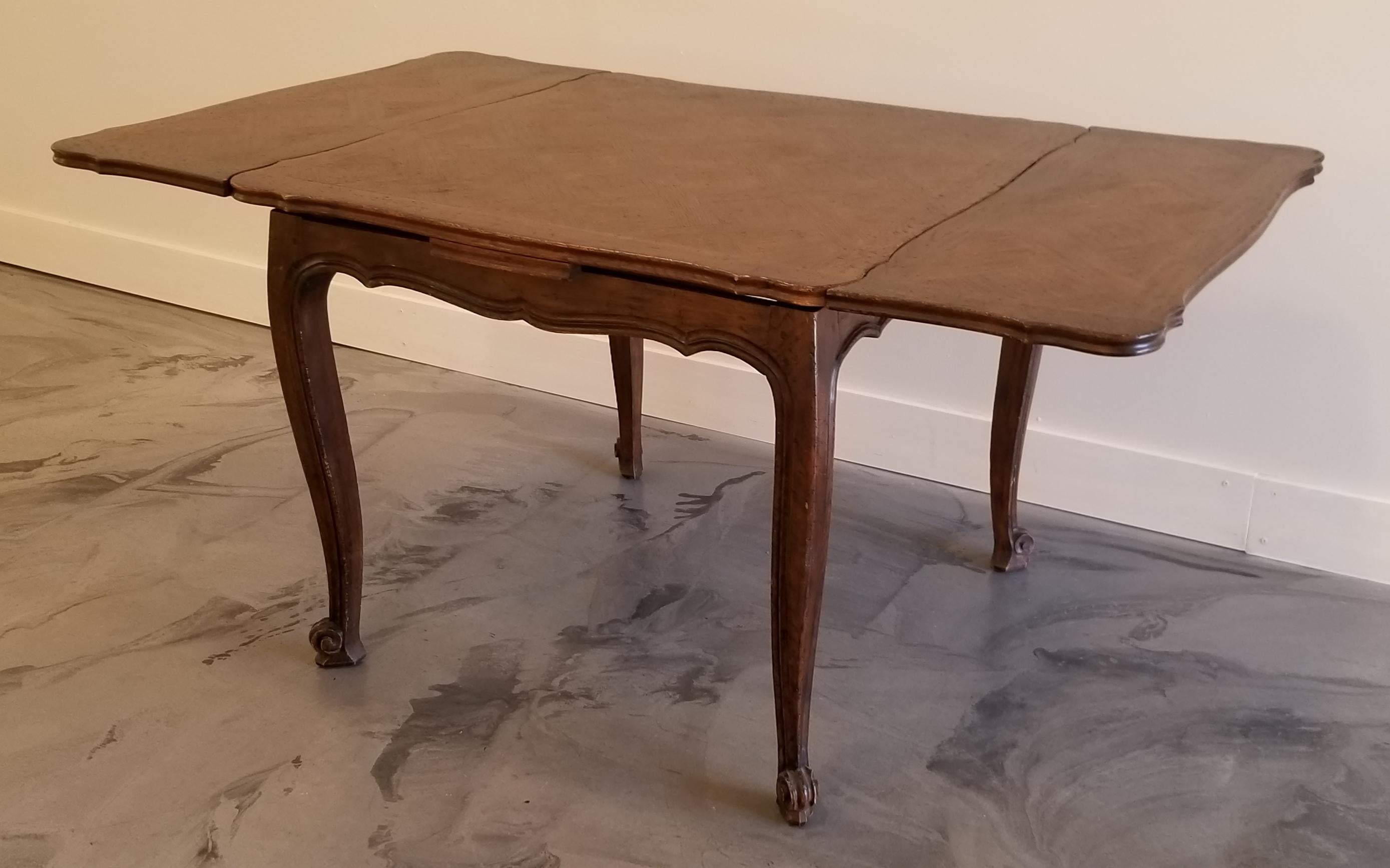 An early 20th century French provincial draw leaf dining table with oak parquet top, matching parquet leaves and hand carved scroll legs. Uncommon diminutive size that would work well as a dinette table, breakfast room or small dining area. Fully