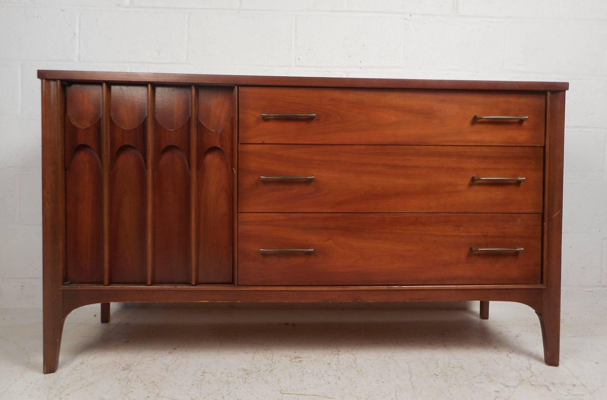 This beautiful vintage modern sideboard features three hefty drawers and a large storage compartment with a shelf. A vintage walnut finish, unique metal drawer pulls, and sculpted cabinet handles add to the allure. Quality craftsmanship with a