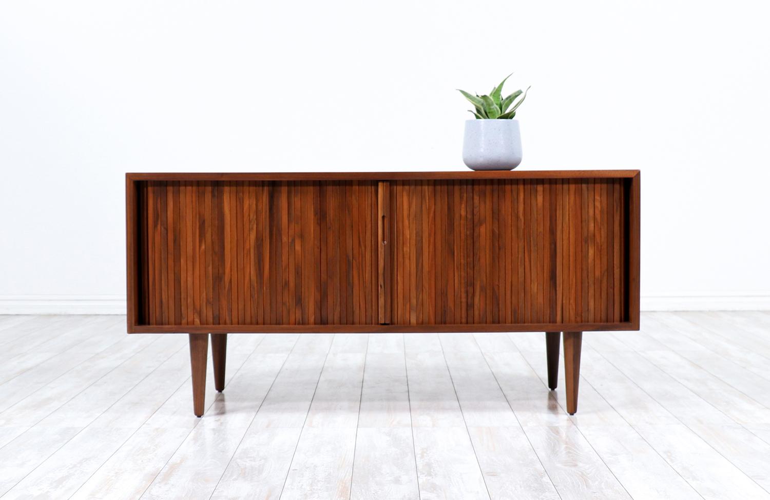 Compact tambour-door credenza designed by Milo Baughman for Glenn of California in the United States circa 1950’s. Impeccably crafted with walnut wood and newly refinished by our skilled craftsmen, this credenza features a tambour doors with