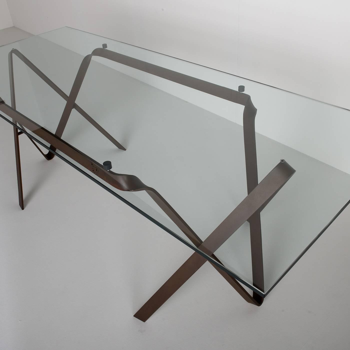 Harmoniously balancing a sculptural aesthetic and functionality, this boasts a rectangular top fashioned of extra clear, tempered glass seemingly floating atop a base made of crossed, hand-forged iron blades with a natural rust finish. This