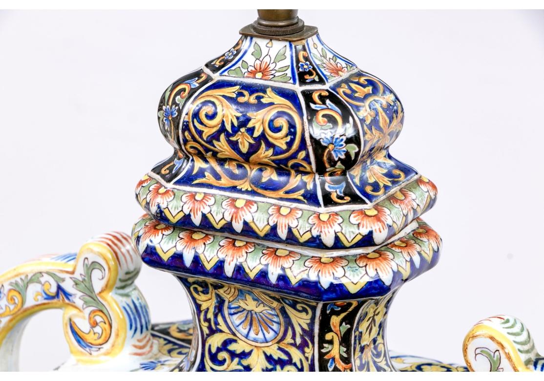 Coppia compatibile di urne con coperchio in ceramica maiolicata dipinte a mano con bouquet floreali, cesti, volute foliate, cornucopie e motivi geometrici. in blu, oro, bianco e ruggine. Le lampade sono dotate di manici sagomati, doppio attacco per