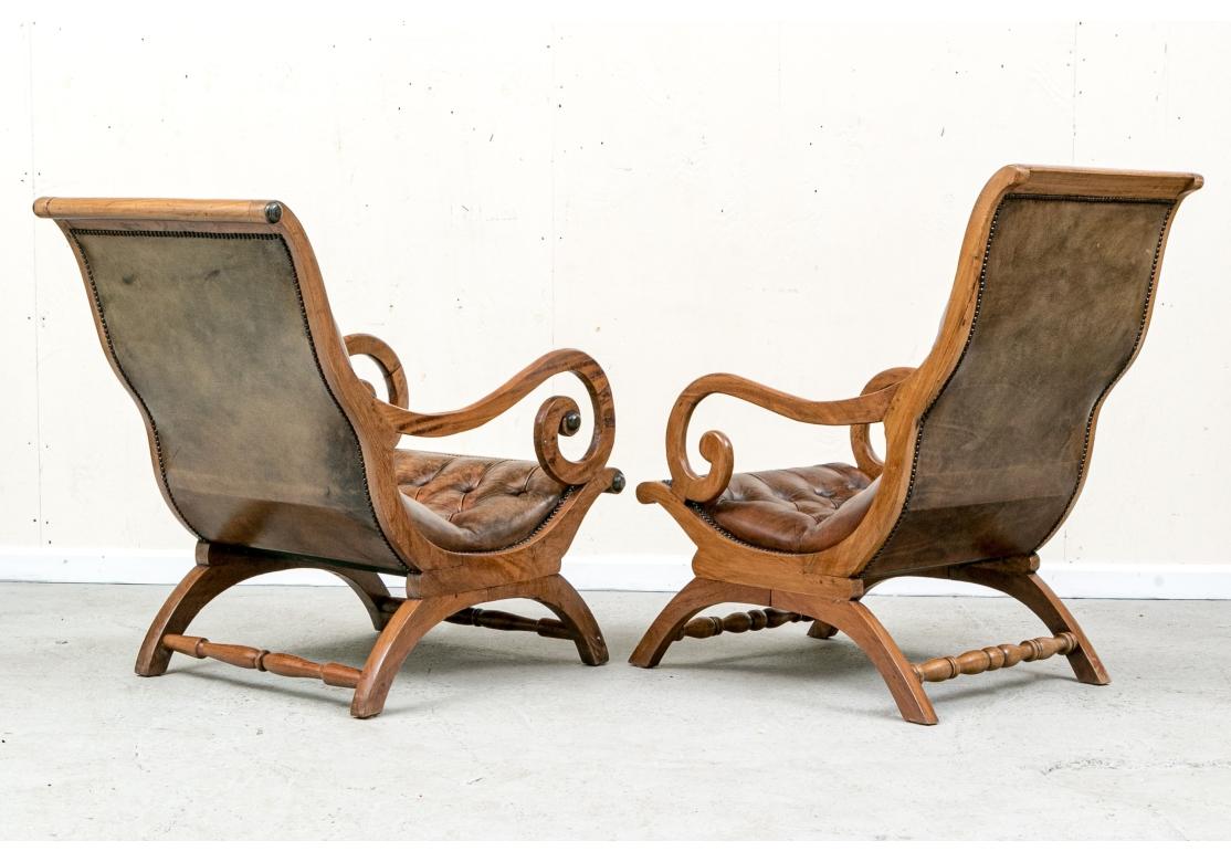 Paire de chaises Lolling vintage présentant un luxueux revêtement en cuir à boutons profonds dans une riche teinte châtaigne avec des touches de rouge et d'or, accentuées par des clous en laiton. Le cadre en acajou massif présente un design incurvé