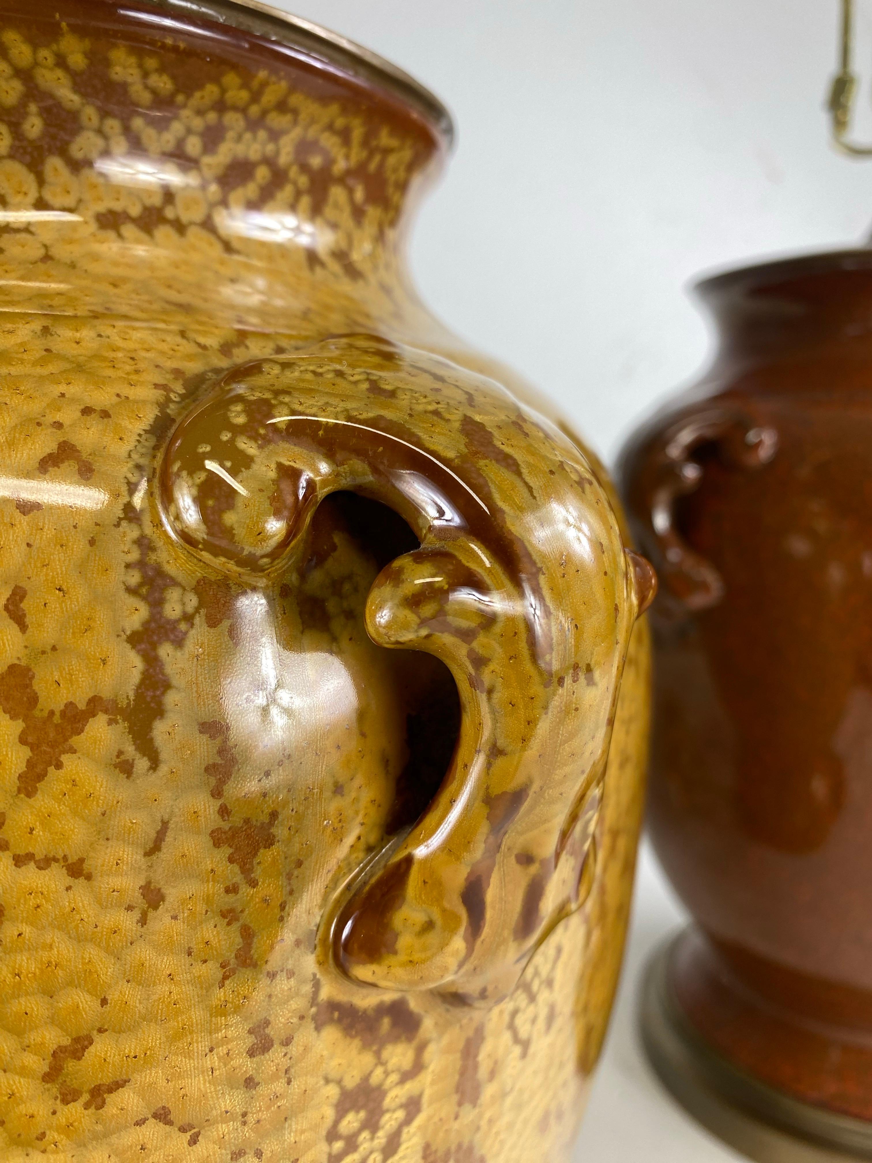 This is a complementary pair of French country style pottery table lamps. These handsome lamps are identical with the exception of the color. One lamp is a burnt rust and brown and the other is a mustard yellow with Amber. The lamps have four