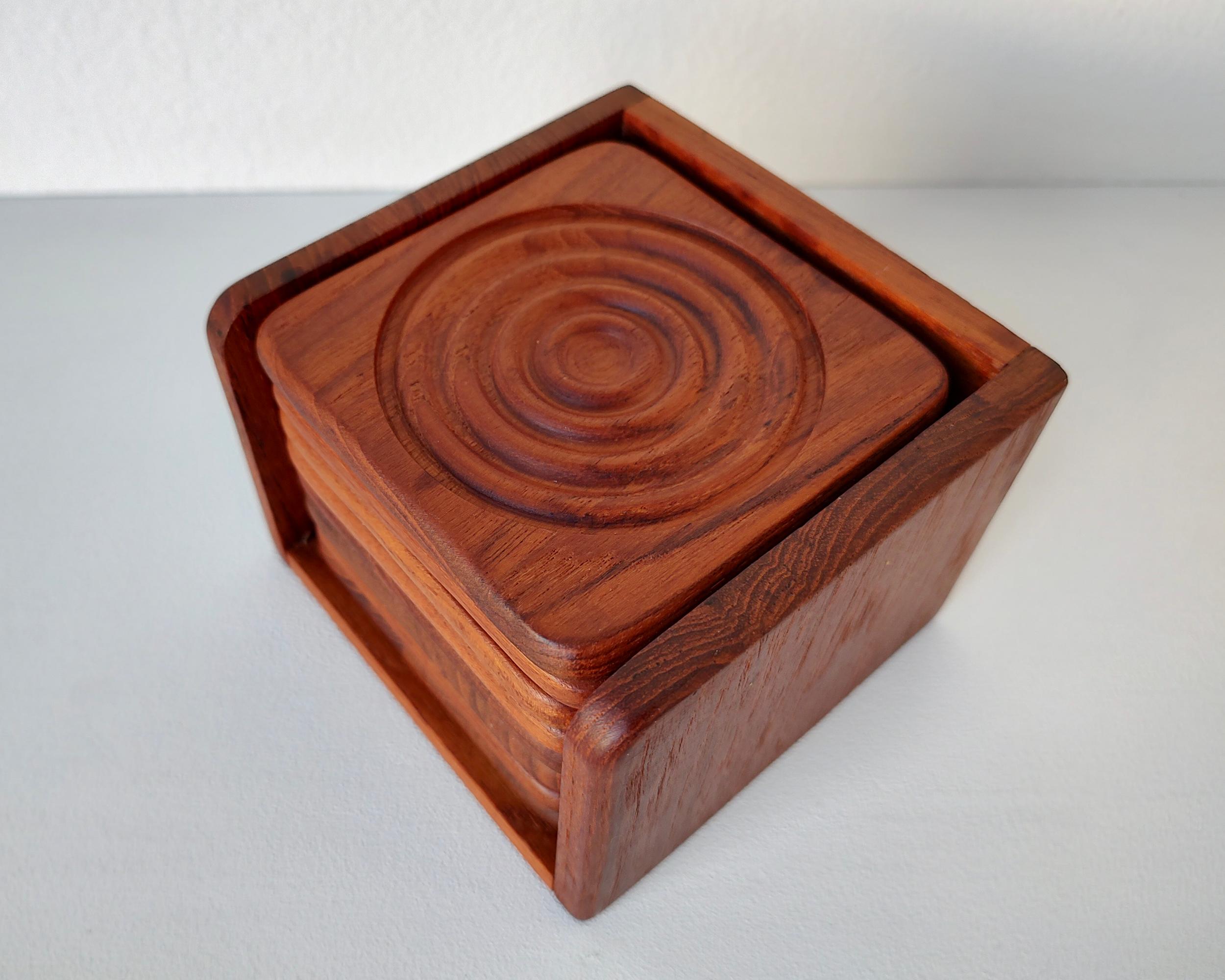 Set of eight (8) solid teak coasters with caddy. Carved ripple pattern catches condensation and prevents glasses from getting stuck to the coaster. Wood has been conditioned, light wear consistent with vintage age.