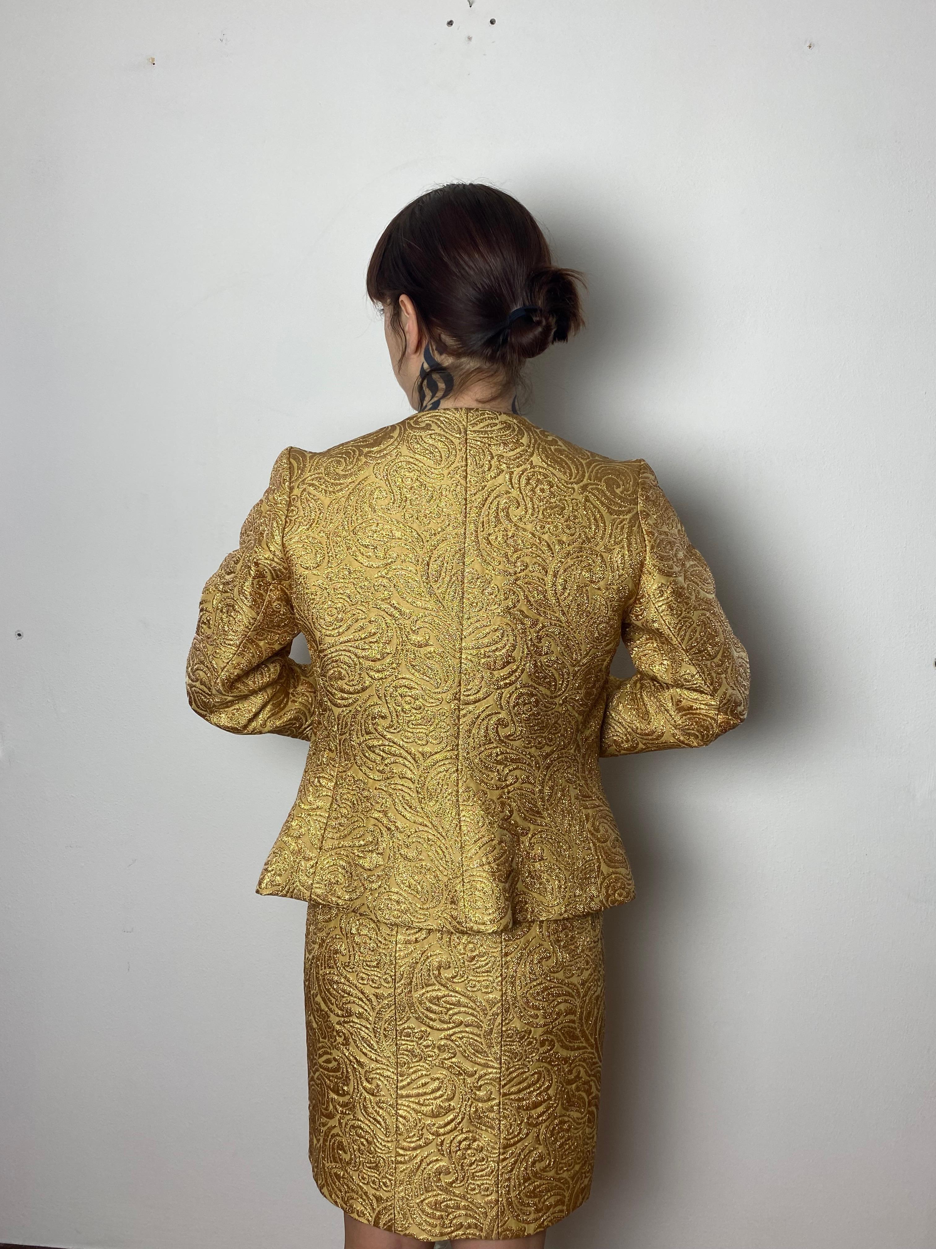 Schimmernde Brokatjacke mit goldenem Jacuqrd-Muster von Saint Laurent Rive Gauche. Geformte, taillierte Silhouette mit hohem Ausschnitt Strukturierter, floraler Brokat 7-Knopf-Öffnung vorne mit mattgoldfarbenen Drehknöpfen Geformter Prinzesssaum mit