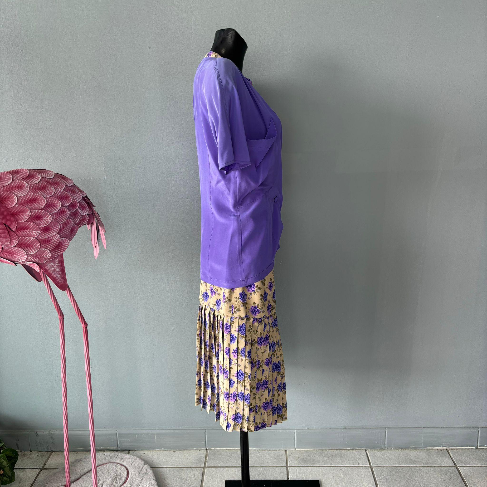 Completo in seta Genny anni 80 composto da camicia e gonna 
La camicia doppiopetto viola con tasche frontale ha il bordino che riprende il motivo floreale della gonna
La gonna per metà a pieghe dona un tocco di leggerezza all'outfit
Condizioni