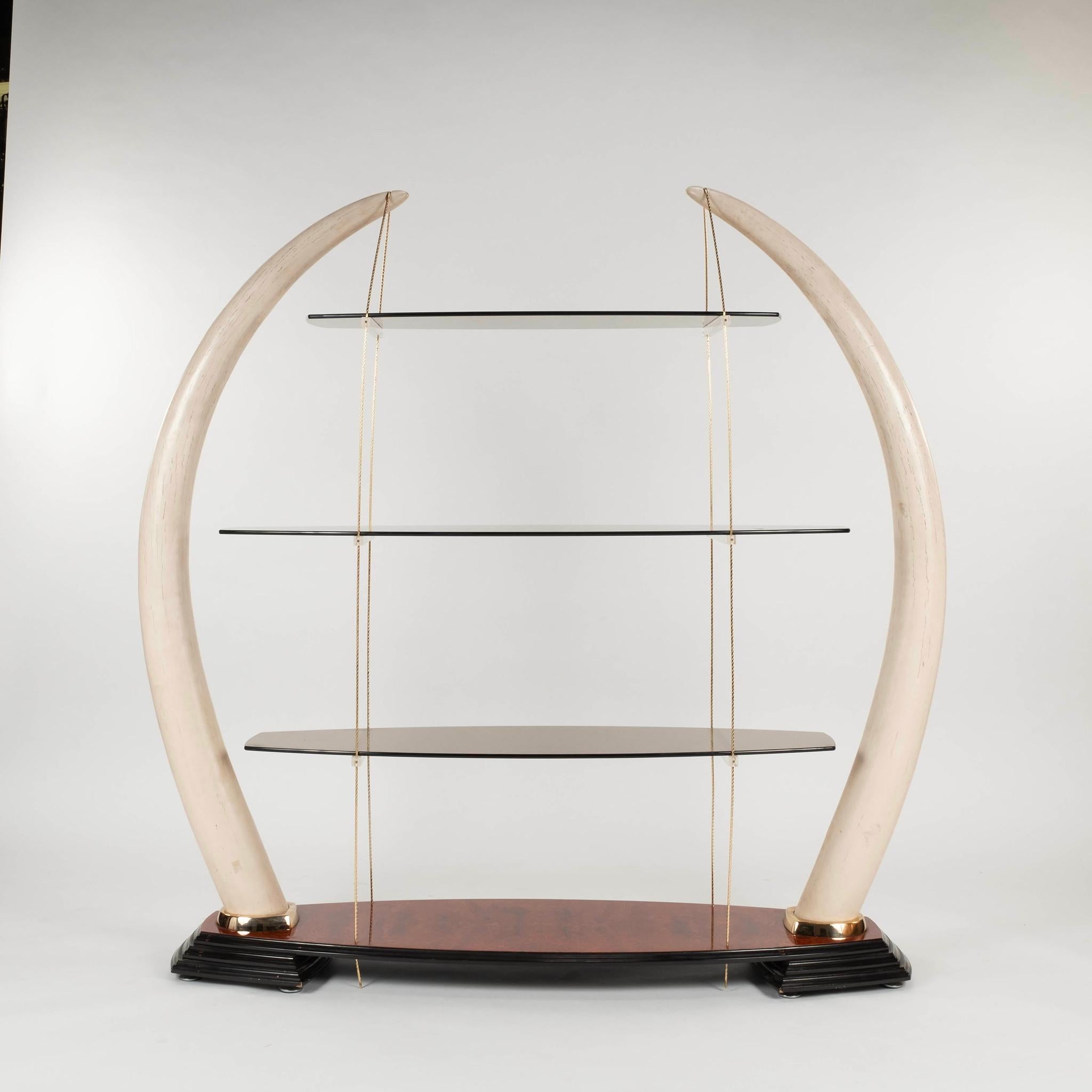Élégante étagère espagnole des années 1970 en verre et en défense d'éléphant composite. De monumentales fausses défenses d'éléphant avec une corde en métal doré sont montées sur un socle en bois de ronce laqué qui suspend trois étagères en verre