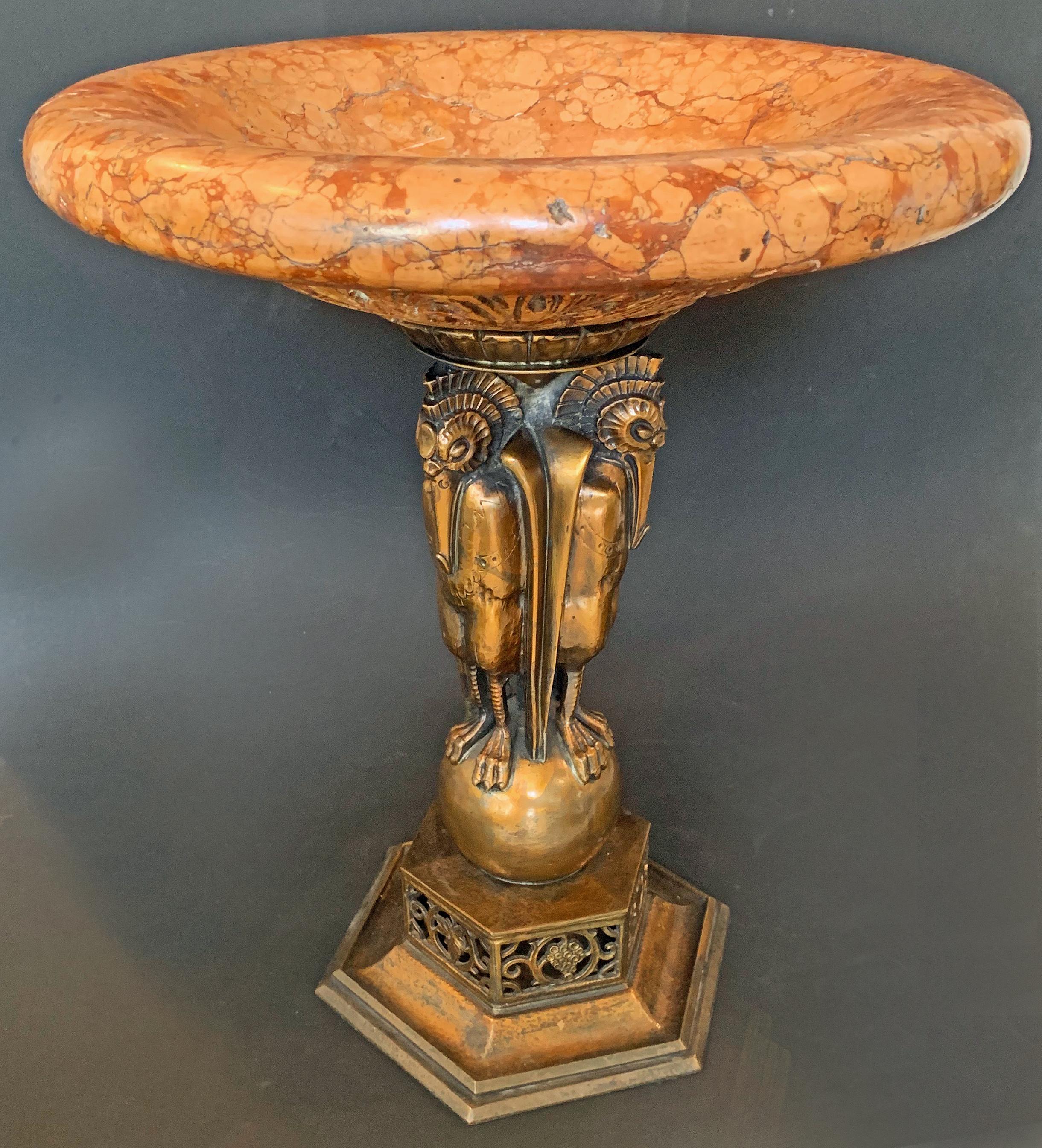 Unique and masterfully crafted, this monumental Art Deco compote features a group of stylized storks supporting a coral-hued marble bowl, carved on its underside with interlocking acanthus leaves. This piece is unique, and shows Oscar Bach's work at
