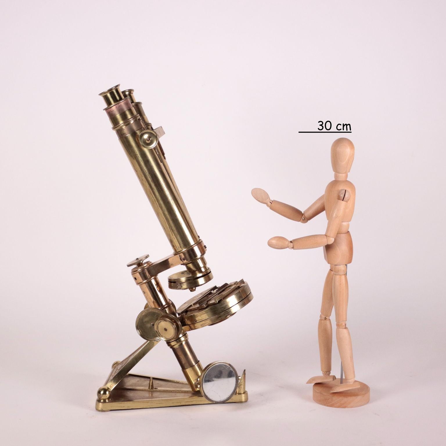 Compound binocular microscope mounted on a triangular base, serial number 6746, in lacquered brass. The rod, which supports the double optical tube, the circular table and the mirror, can be set at different angles. The rough focus is done through