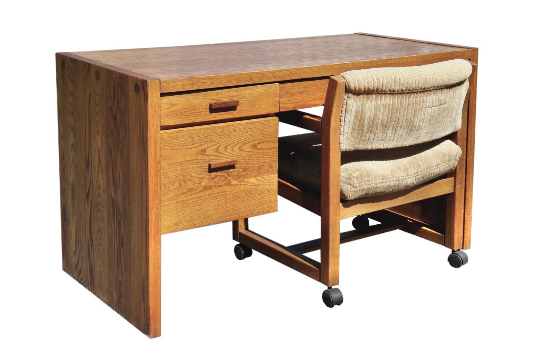A mid century writing desk and matching chair made by Conant Ball. Made of solid ash with beautiful grain. Sleek lines throughout with three simple drawers and waterfall sides. The desk chair has open arms that fit neatly underneath the desk. The