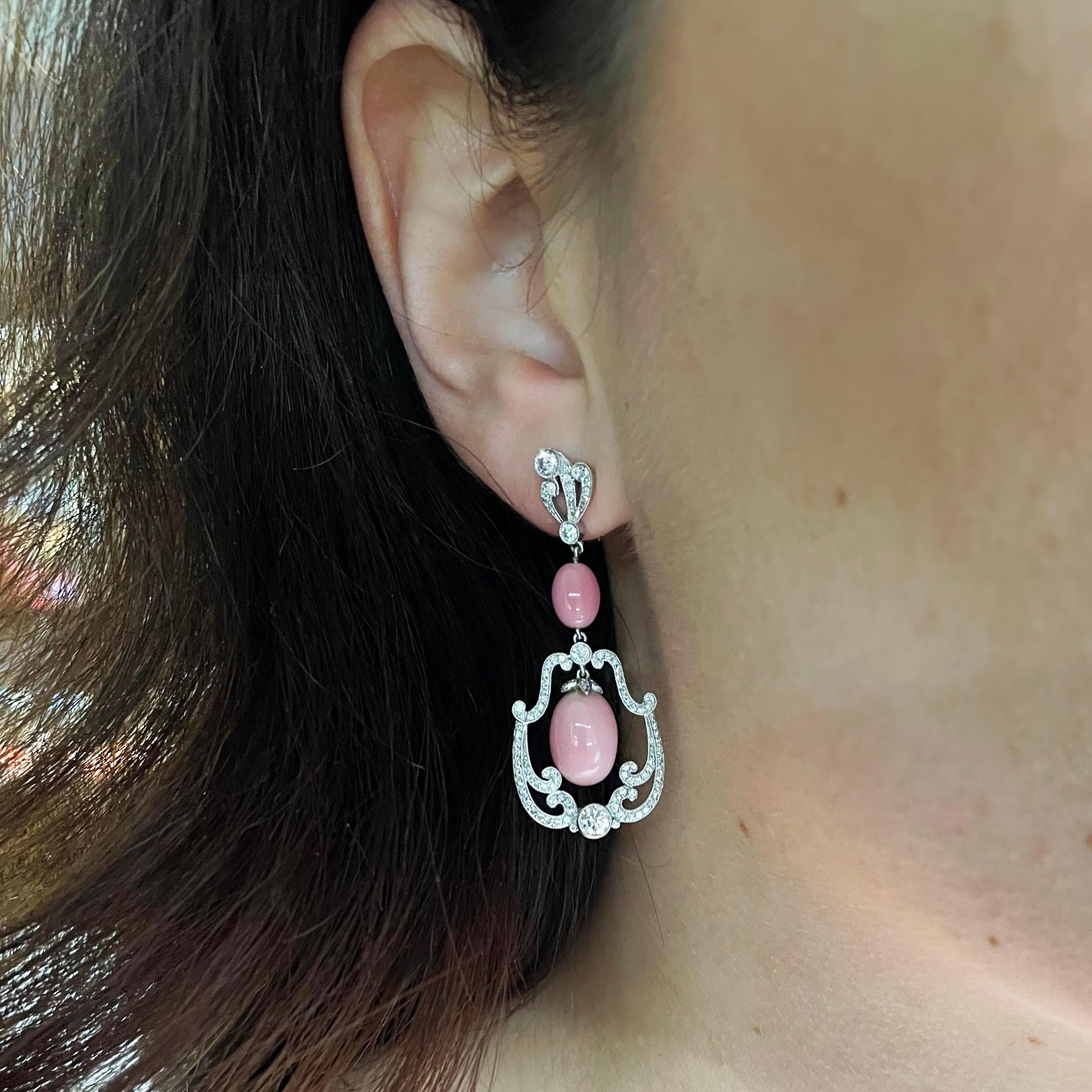 Ein Paar moderne Tropfenohrringe, bestehend aus einem Muschelperlen-Anhänger, der in der Mitte eines diamantbesetzten Rahmens aufgehängt ist, darüber eine kleinere Muschelperle und ein diamantbesetztes Fächermotiv, alles in Platin gefasst.

Das