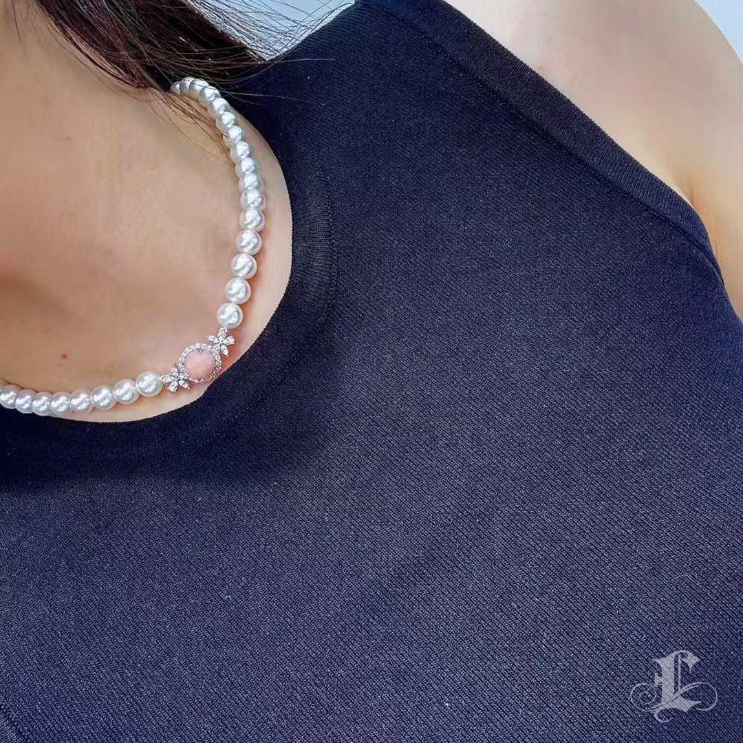 Création rare et romantique, ce collier présente une perle de conque sans défaut de 5,85ct dans une chaude teinte rose-orange, parfaitement ronde et richement lustrée. La pièce centrale est entourée de motifs floraux sertis de diamants, menant à un
