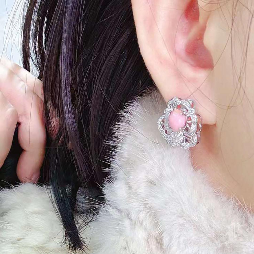 Un chef-d'œuvre de rareté et de grâce - une perle de conque de près de cinq carats, brillant d'une douce flamme rose, repose au cœur de pétales de diamants. Le design floral incarne l'éternité, où chaque courbe chatoyante capture la poésie de la