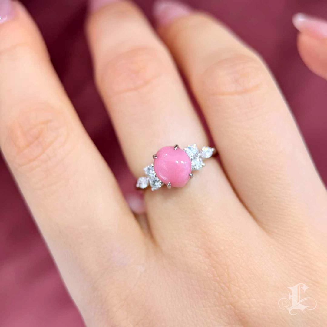 Cette magnifique bague en perles de conque est ornée d'une pierre précieuse de 2,6 carats, d'un rose flamant vif, dont la surface est animée de motifs de flammes saisissants, visibles à la lumière naturelle. Sertie en platine et rehaussée de 0,49ct