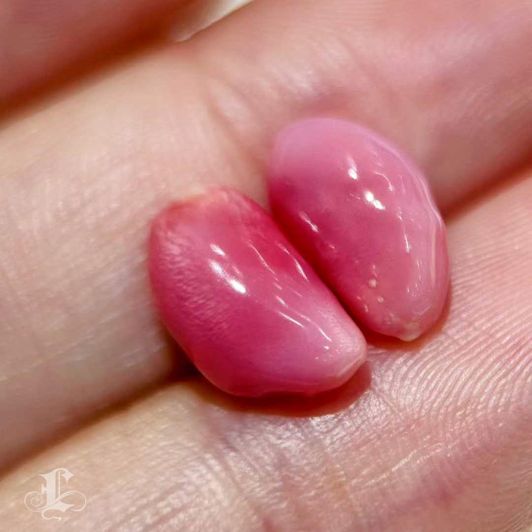 Un par de perlas de concha naturales, raras y bellamente emparejadas, elegantemente modeladas en forma de grano de arroz, cada una de ellas resplandeciente con tonos rosas saturados y espectaculares dibujos de llama en toda la superficie. Con un