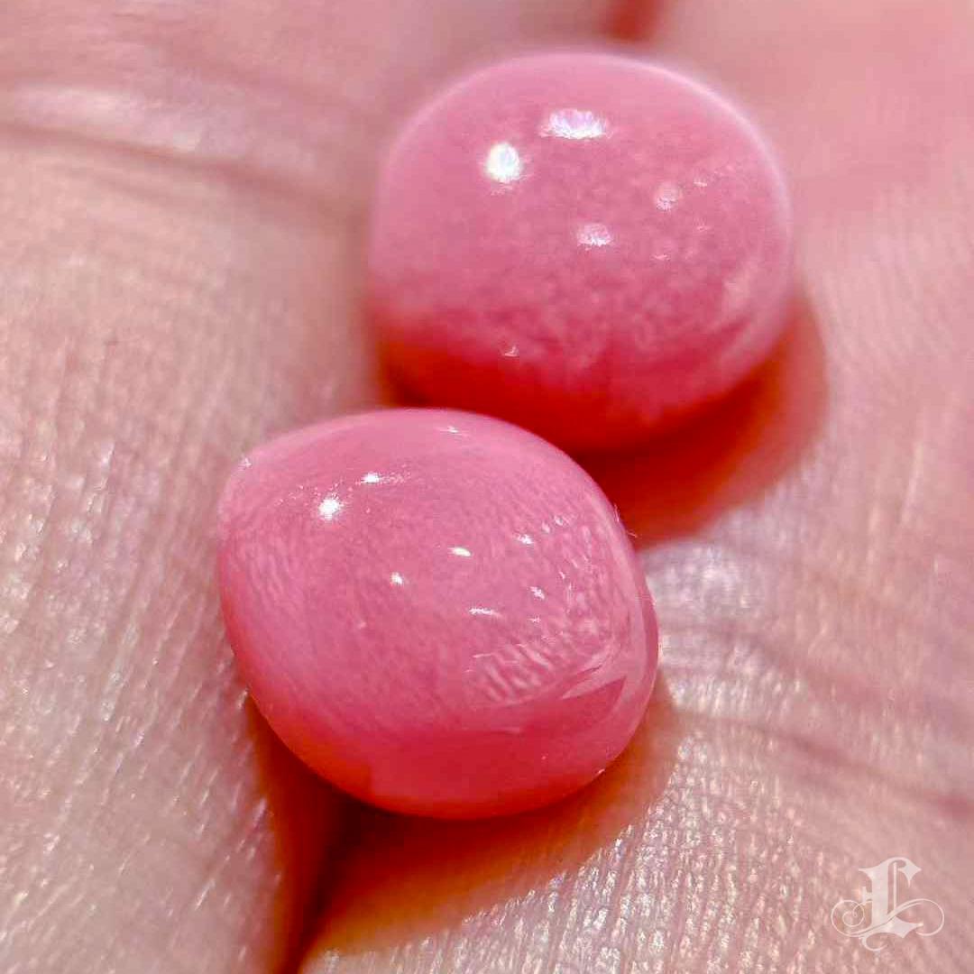 An exceptional pair of natural conch pearls, weighing 2.6 and 3.12 carats respectively. Their intense flamingo pink hue is beautifully complemented by distinct flame structures, shimmering with fibrous iridescence across the domed