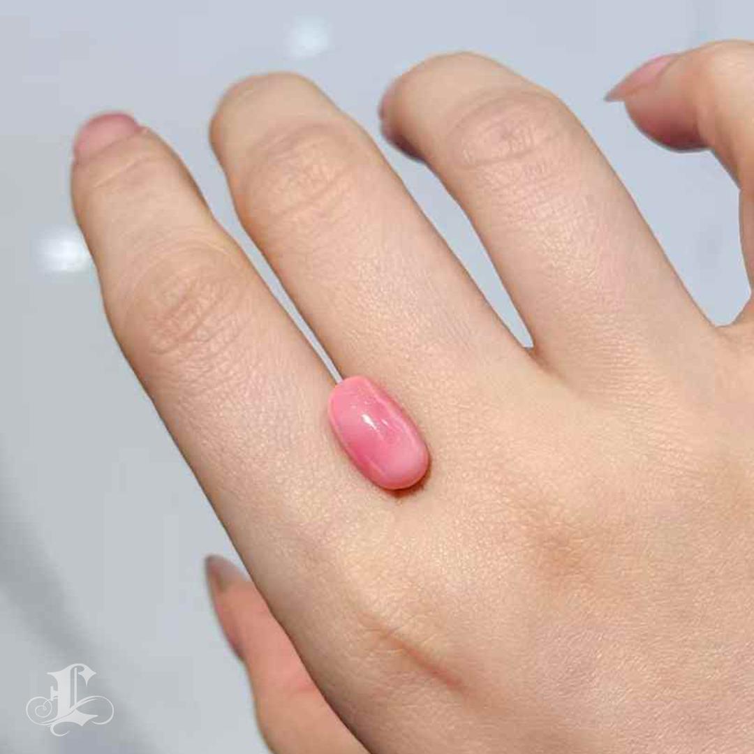 A rare jewel of extraordinary color and presence, this 6.95-carat natural conch pearl glows with a deep pink hue and a mesmerizing flame pattern that dances across its polished cabochon surface. Ovoid in form and richly saturated, this pearl