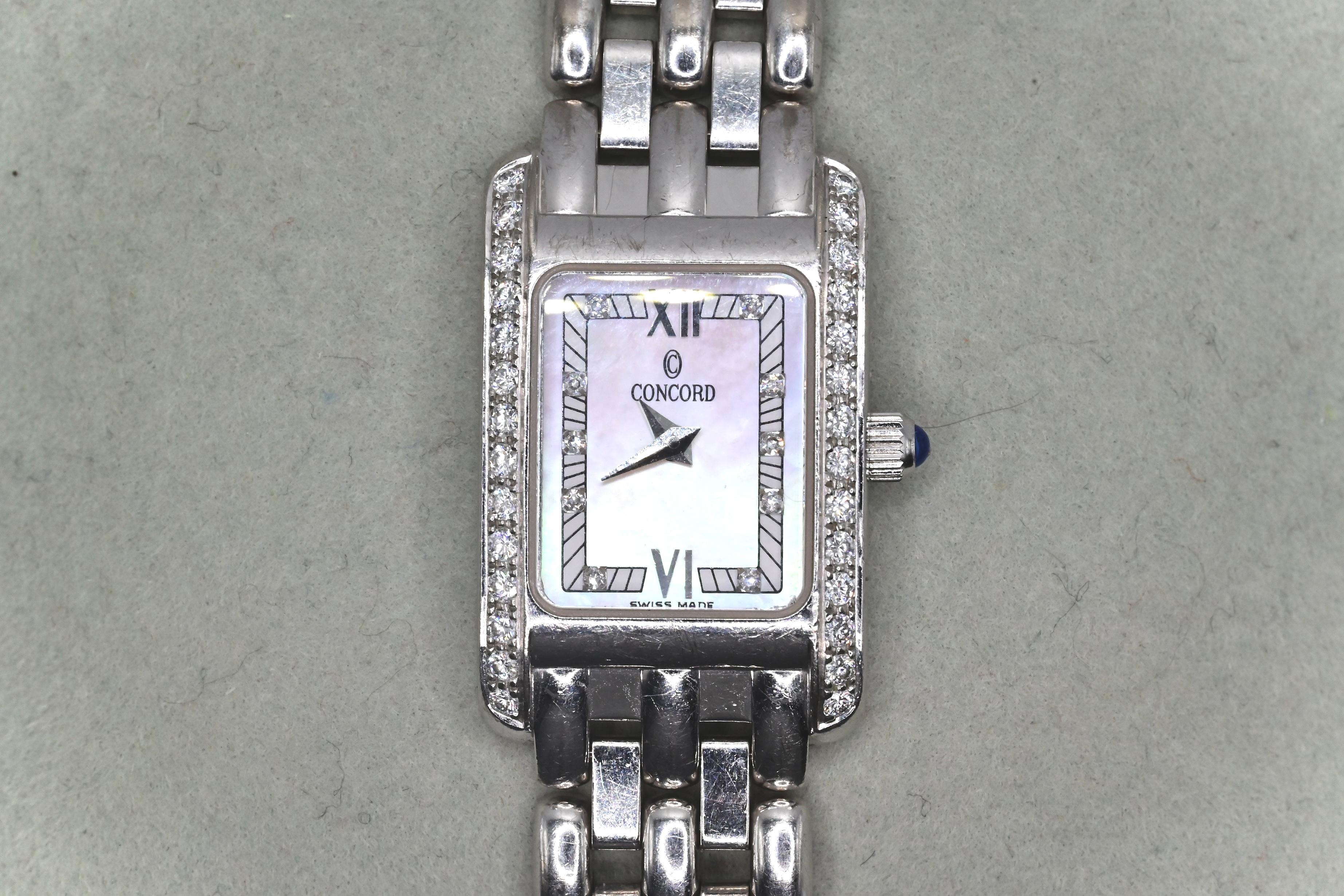 This is a classic pre-owned Concord Veneto ladies wristwatch made with 18k white gold, gorgeous round cut diamonds, and a single blue sapphire on the crown. There’s 28 diamonds encrusted around the bezel, and 10 diamonds placed on certain time