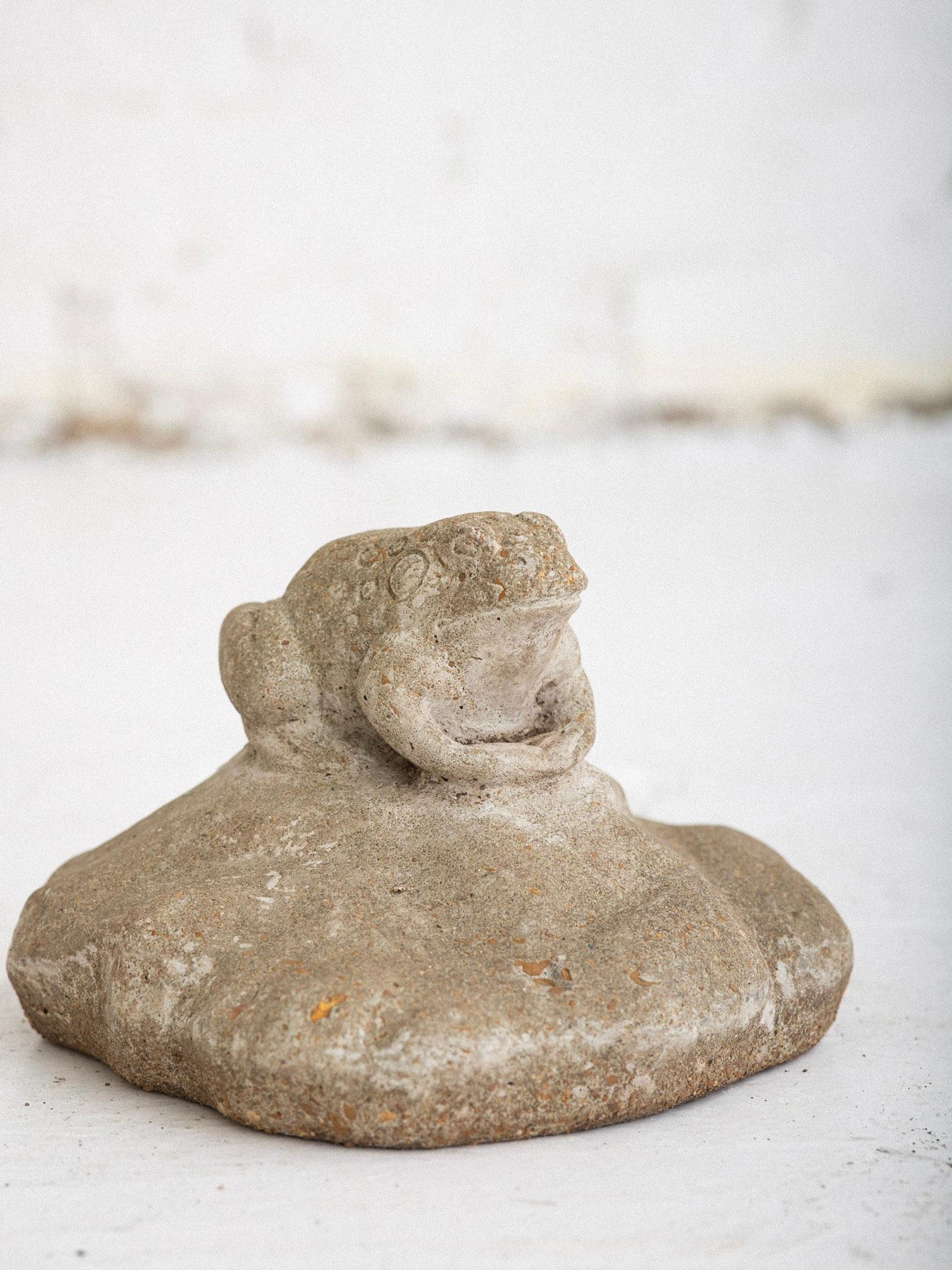 A concrete cast stone sculpture of a frog on lily pad. Flat bottom for sculpture to be placed on garden floor amongst natural elements.