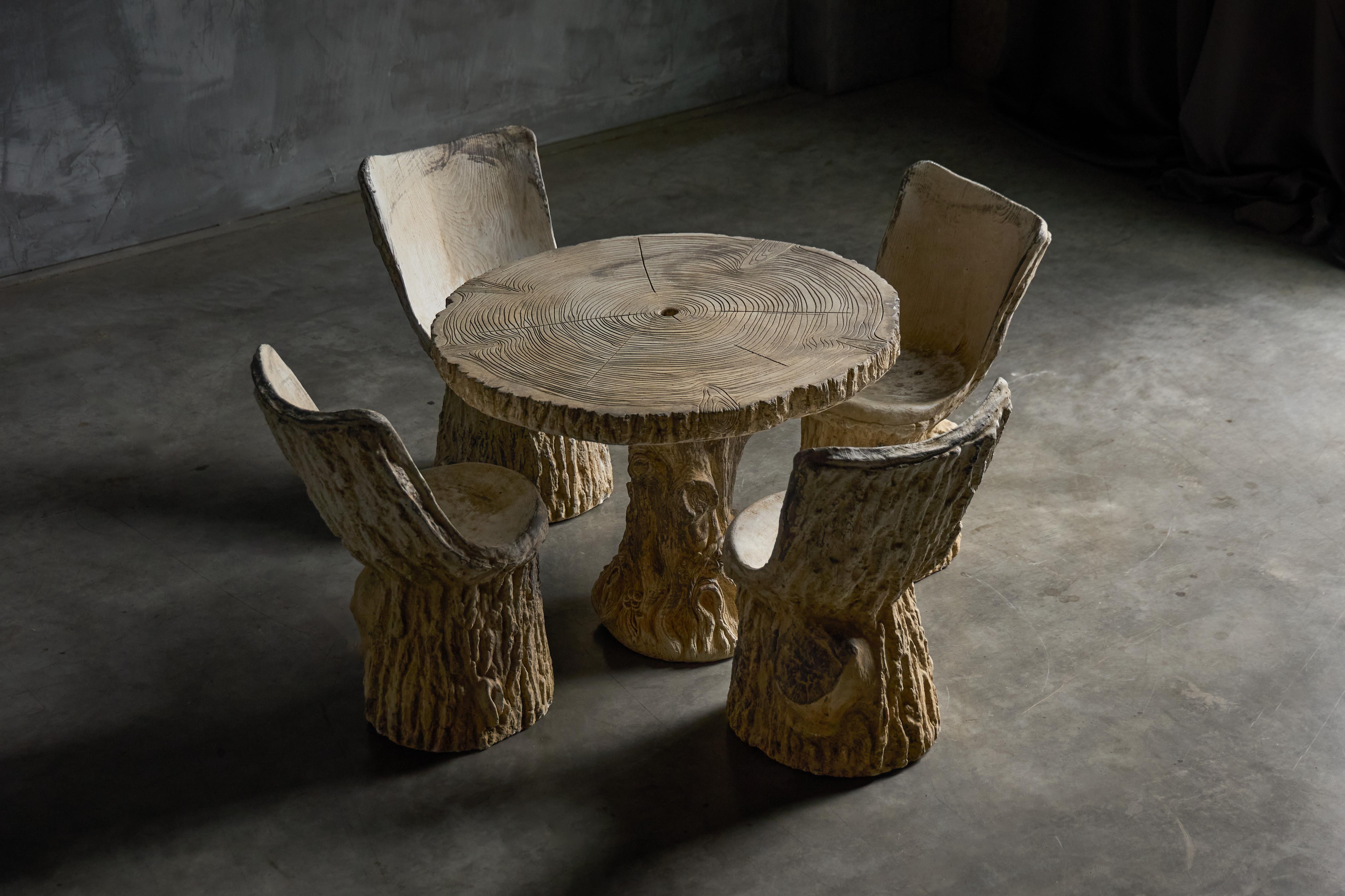 This garden set from 1970s France is cast in concrete with a striking faux-bois finish, mimicking carved tree trunks. Comprising a round table and four chairs, each element is molded with textured bark-like surfaces and gently shaped seats that