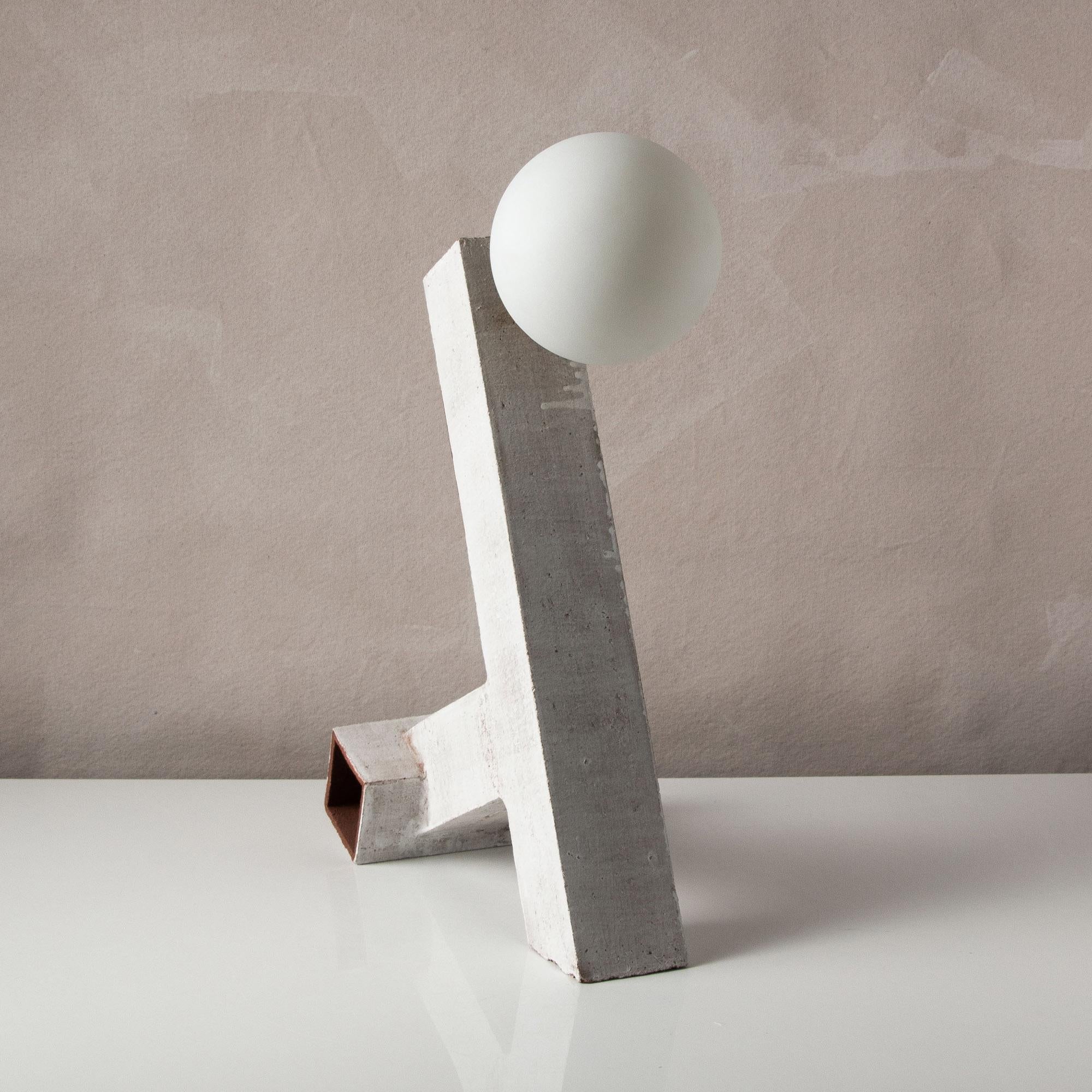 Inspired by midcentury Brutalist architecture and building materials, this playful table lamp balances a strong substantial ceramic base with delicate brass hardware and matte white glass. The angled ceramic base is handcrafted from square tubes of