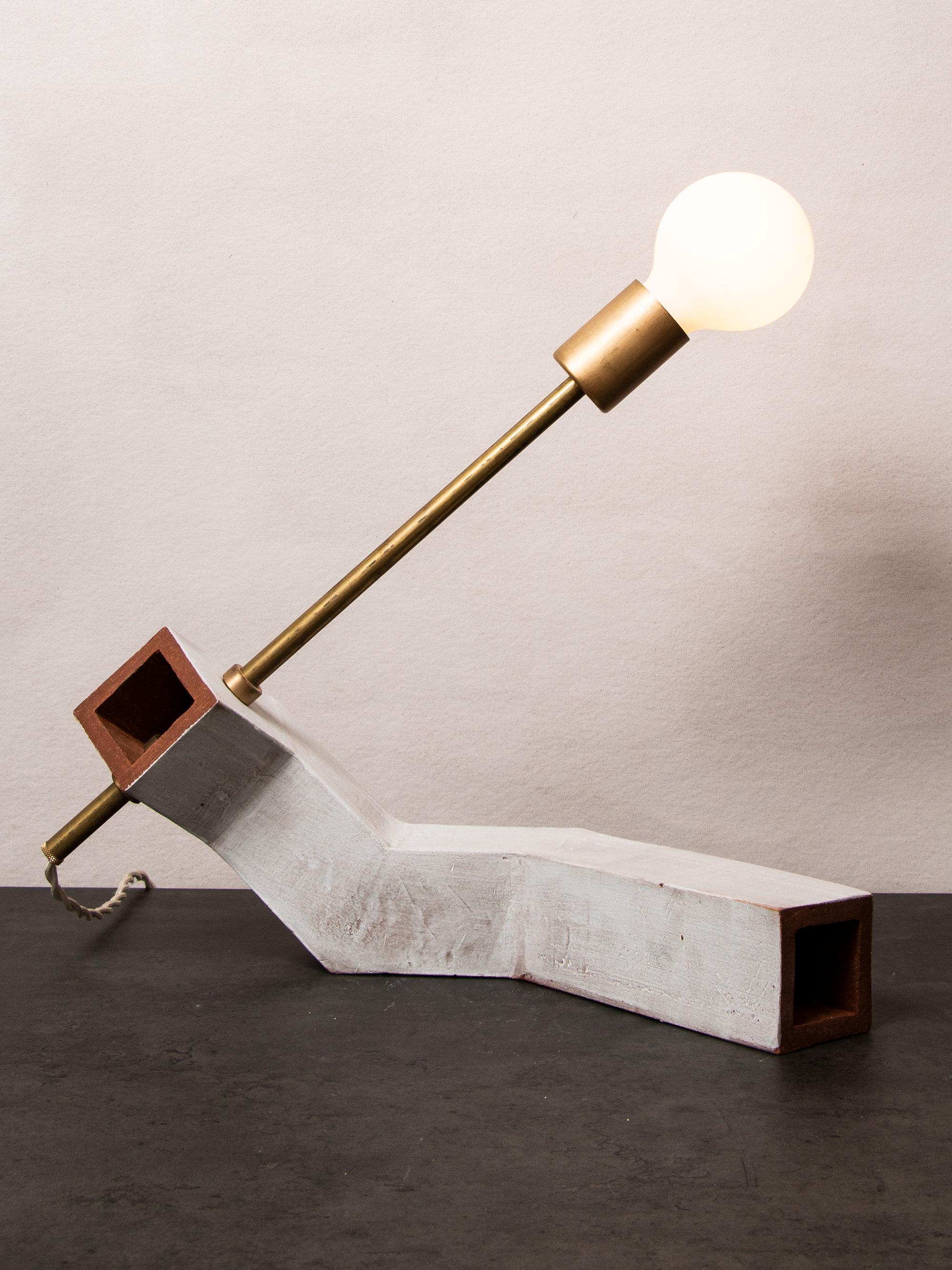 Inspired by midcentury Brutalist architecture and building materials, this playful table lamp balances a strong substantial ceramic base with delicate brass hardware and a modern exposed bulb. The asymmetrical angled rectangular base is handcrafted