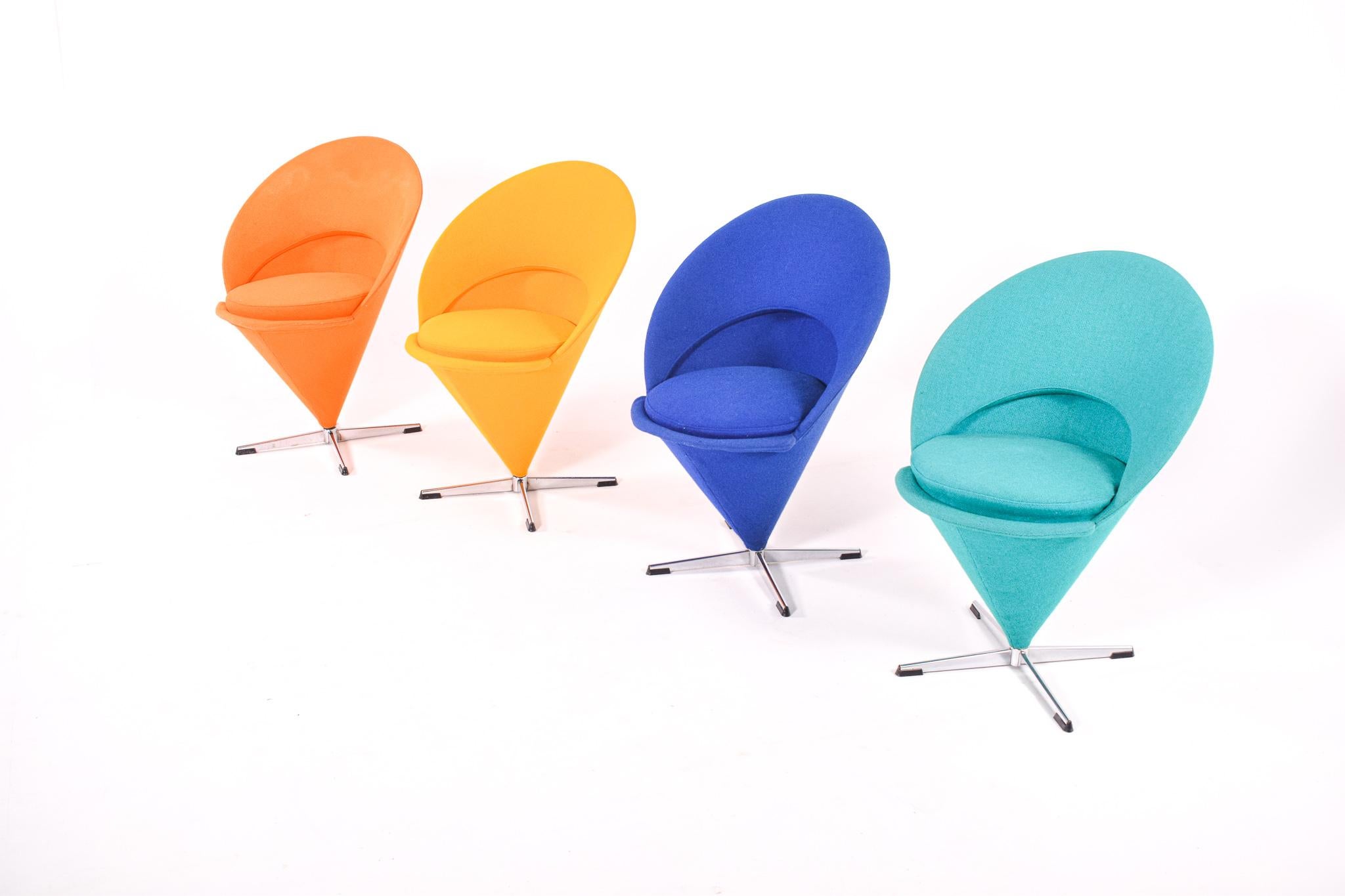 An iconic set of four cone chairs by Verner Panton. The pieces have chrome plated metal bases and are upholstered in blue, green, yellow and orange fabric. Comfortable as side chair or dining chair. Removable seat cushion. Original fabric. Verner