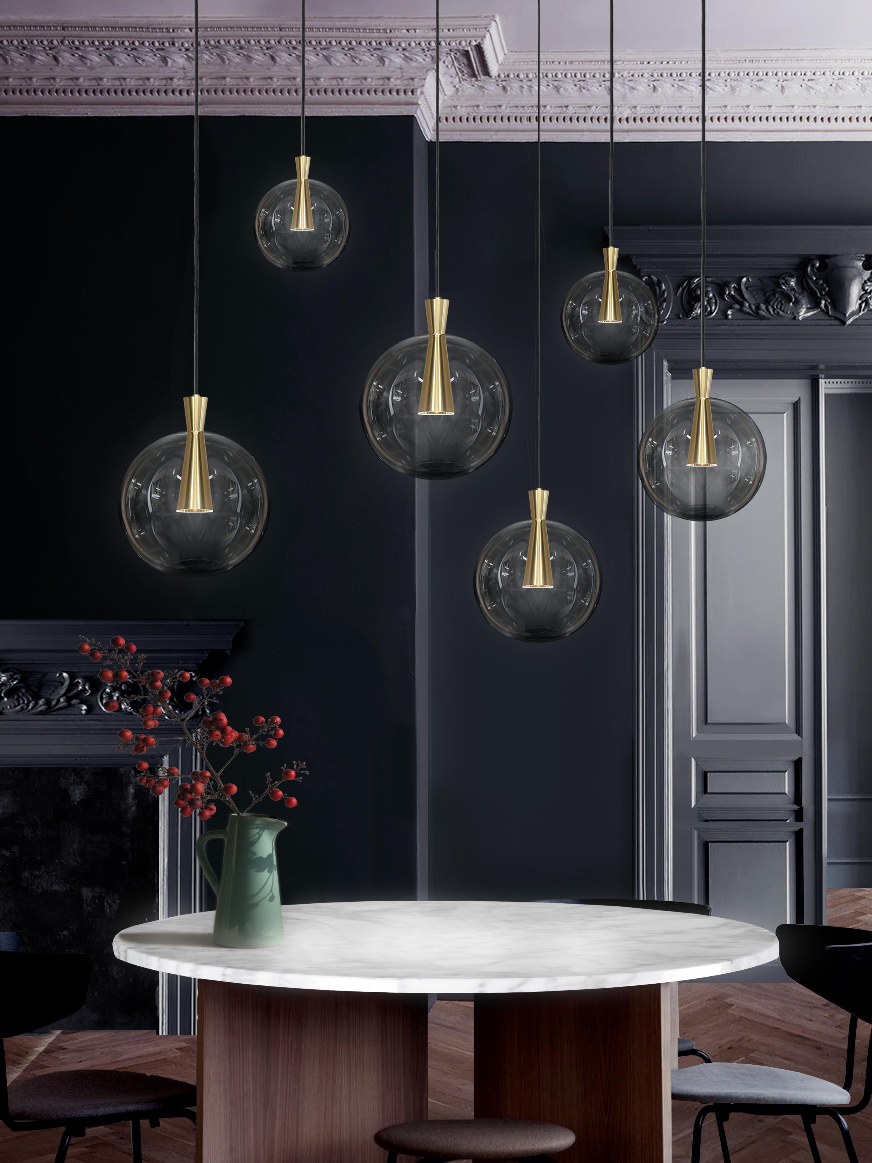 Cone is designed to showcase the beauty and timeless elegance of geometrical symmetry. Each cone is machined from a solid block of brass, with a hand-blown glass shade delicately suspended from the cones apex.