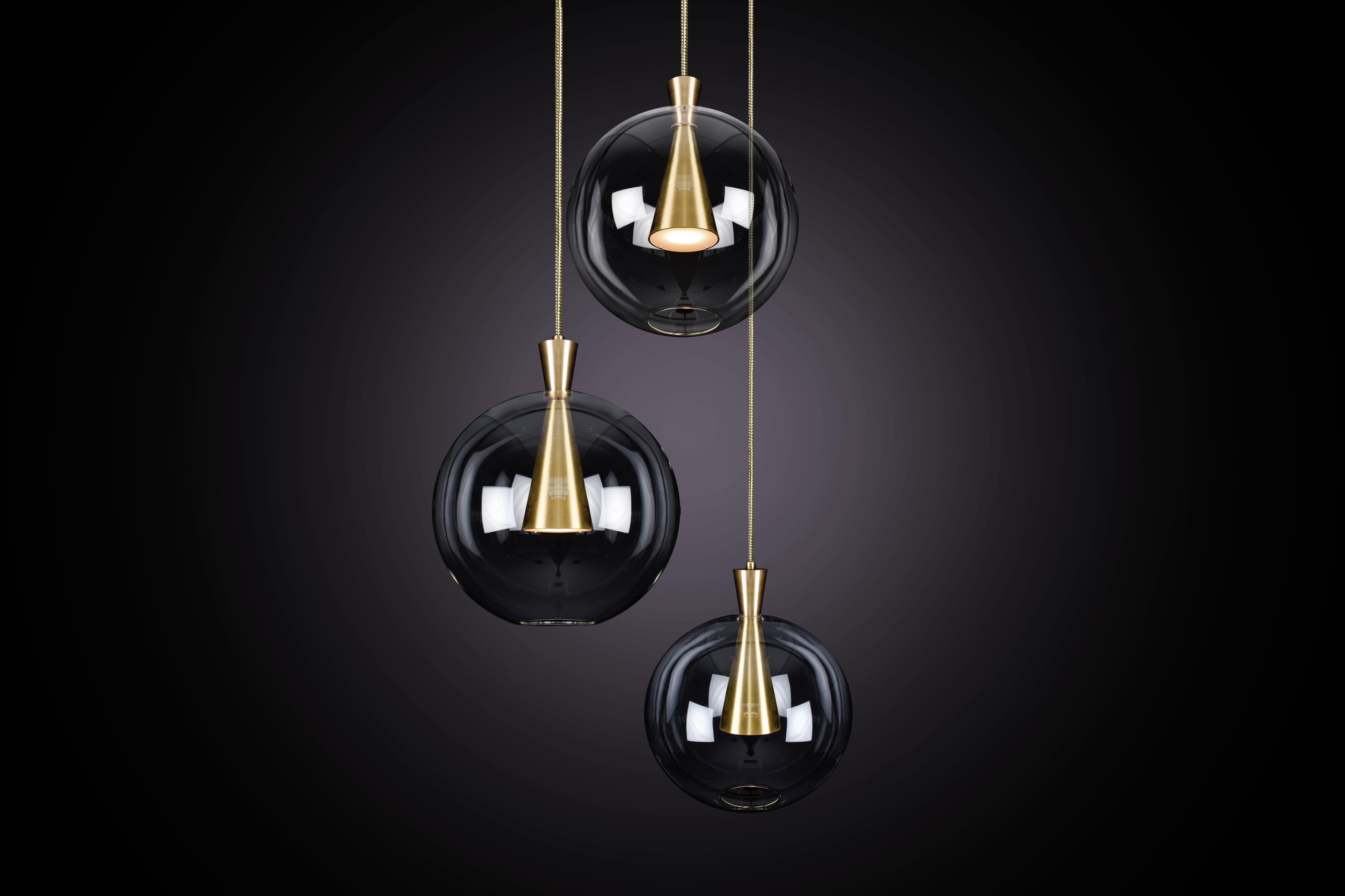 Cone está diseñado para mostrar la belleza y la elegancia atemporal de la simetría geométrica. Cada cono está mecanizado a partir de un bloque macizo de latón, con una pantalla de cristal soplado a mano delicadamente suspendida del vértice de los