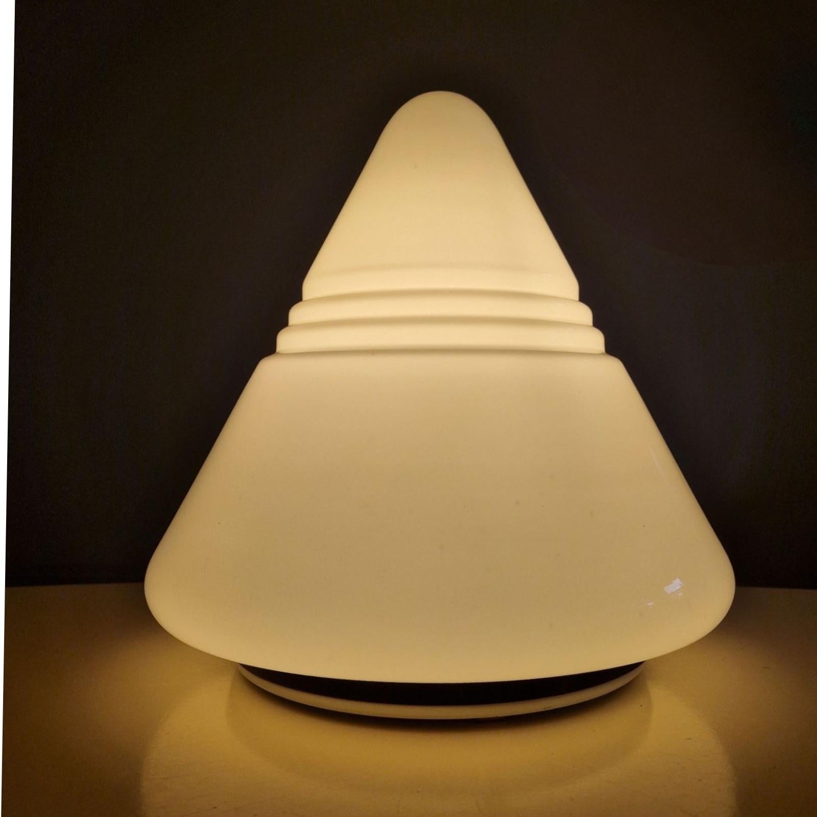 Cone shaped table lamp. The shade is made from opaline glass and the base is made from white lacquered metal with a rubber edge to protect the glass.

The design shows resemblance with the Kilimanjaro lamp by Sergio Asti for Raak.